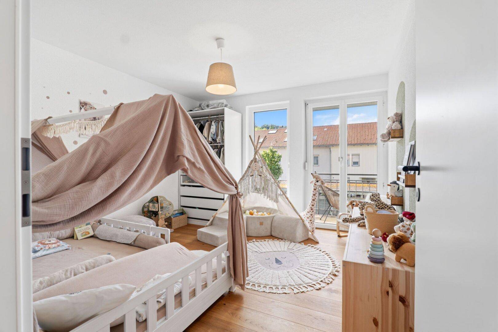 Geräumiges Kinderzimmer mit Holzboden, Spielzelt und Zugang zum Balkon.