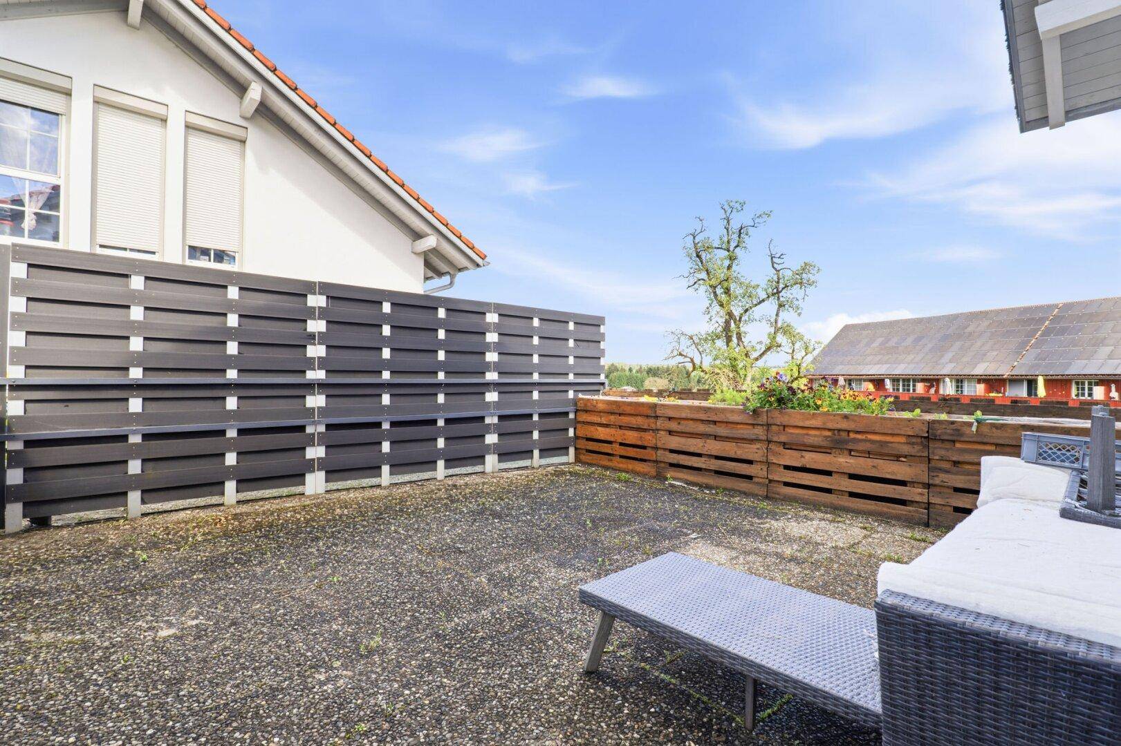 Große Terrasse mit Holzzaun, Liegestuhl und Blick auf die Umgebung.