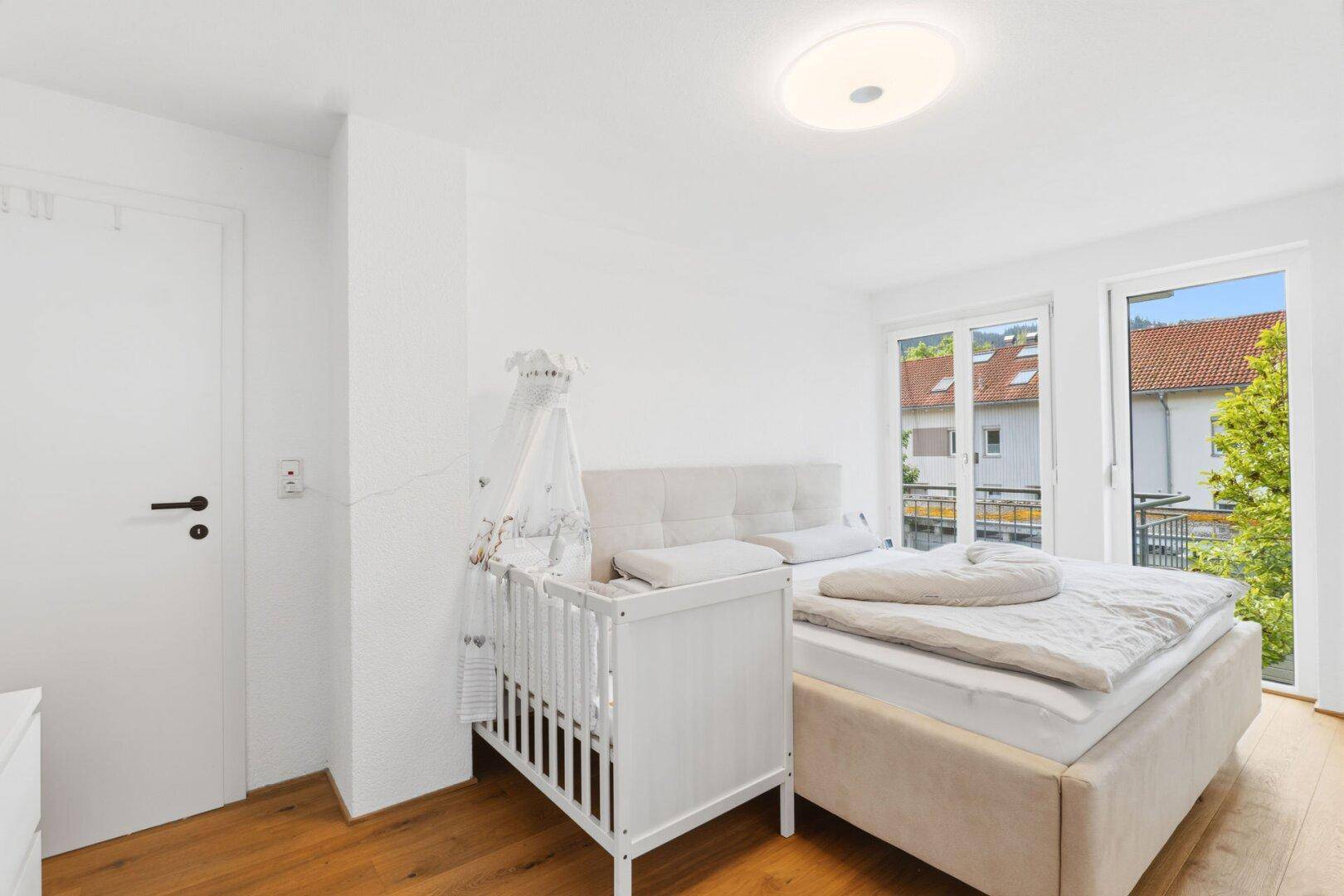 Schlafzimmer mit Doppelbett, Babybett und Zugang zum Balkon.