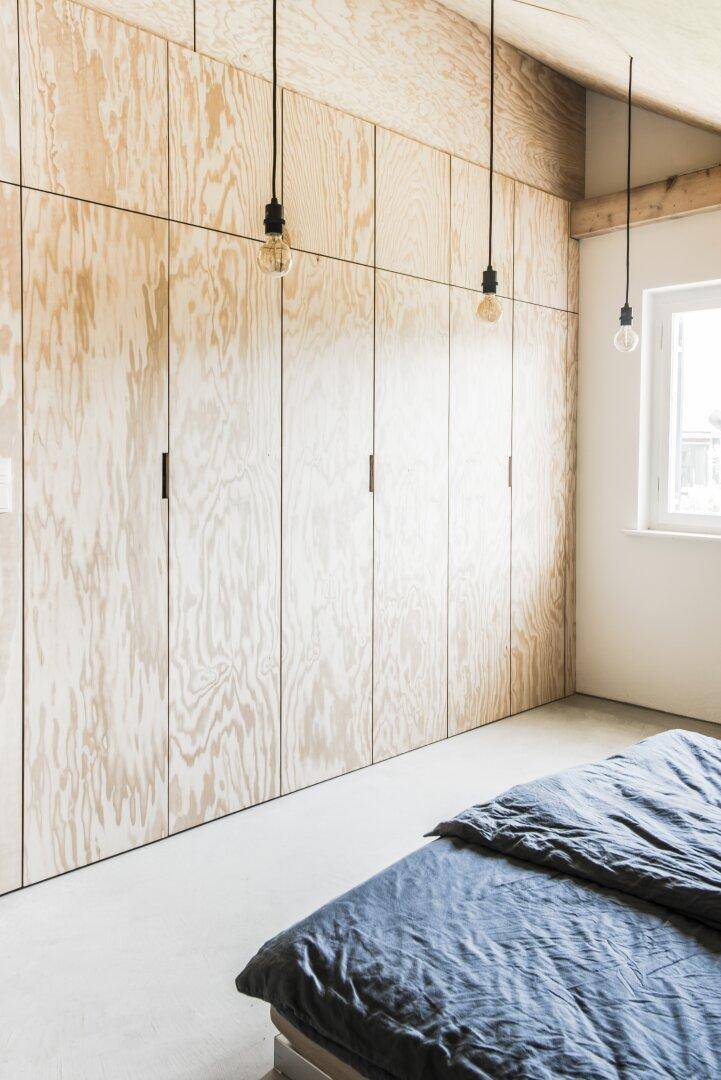 Schlafzimmer mit durchgehender Holzschrankwand, schräger Decke und Fenster.