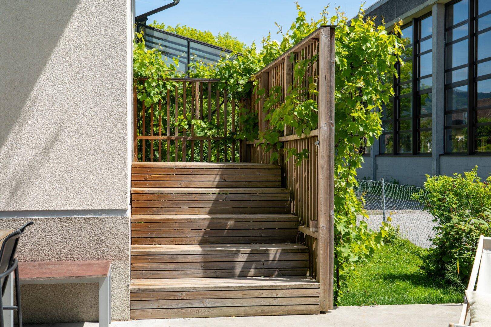 Holztreppe führt von der Terrasse in den Garten, umgeben von Grün.