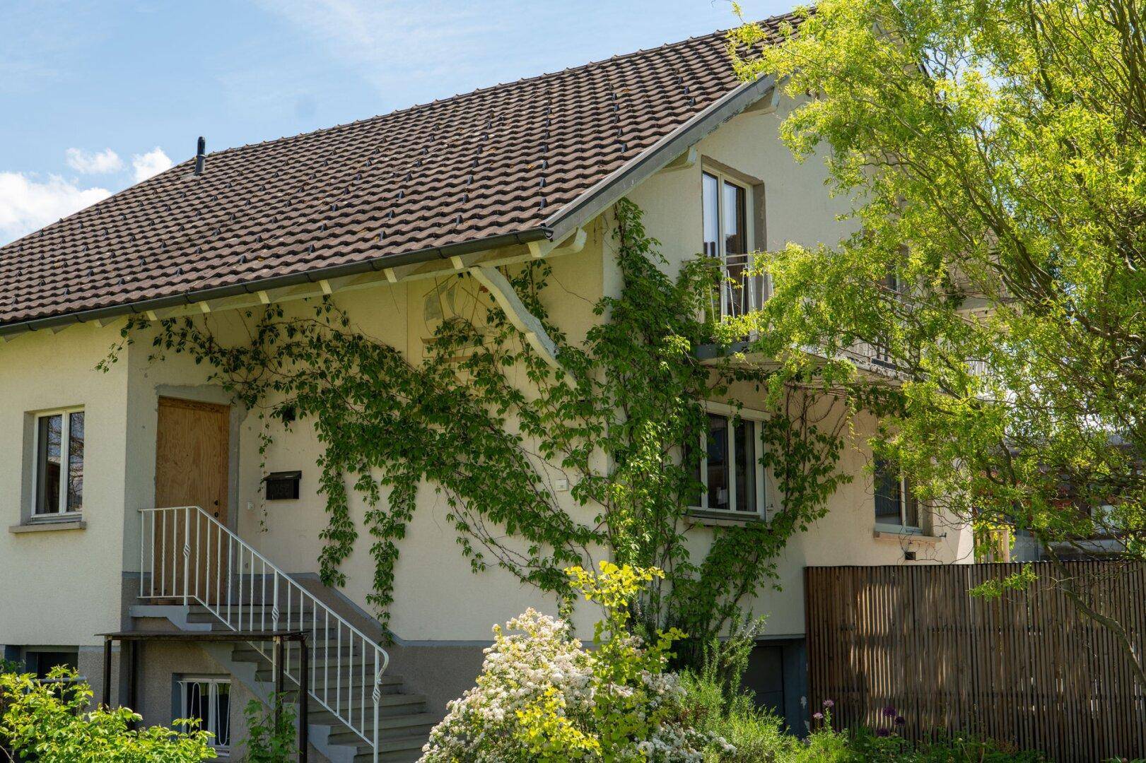 Traditionelles Haus mit Satteldach, bewachsenen Wänden und grüner Umgebung.