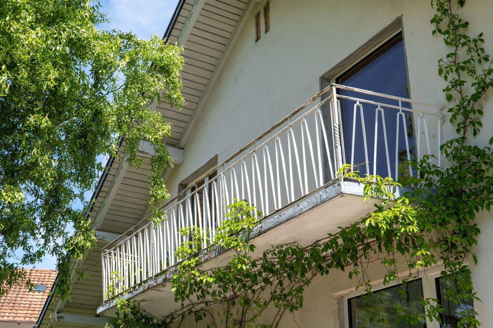 Balkon mit weißem Geländer und üppiger Begrünung an der Fassade.