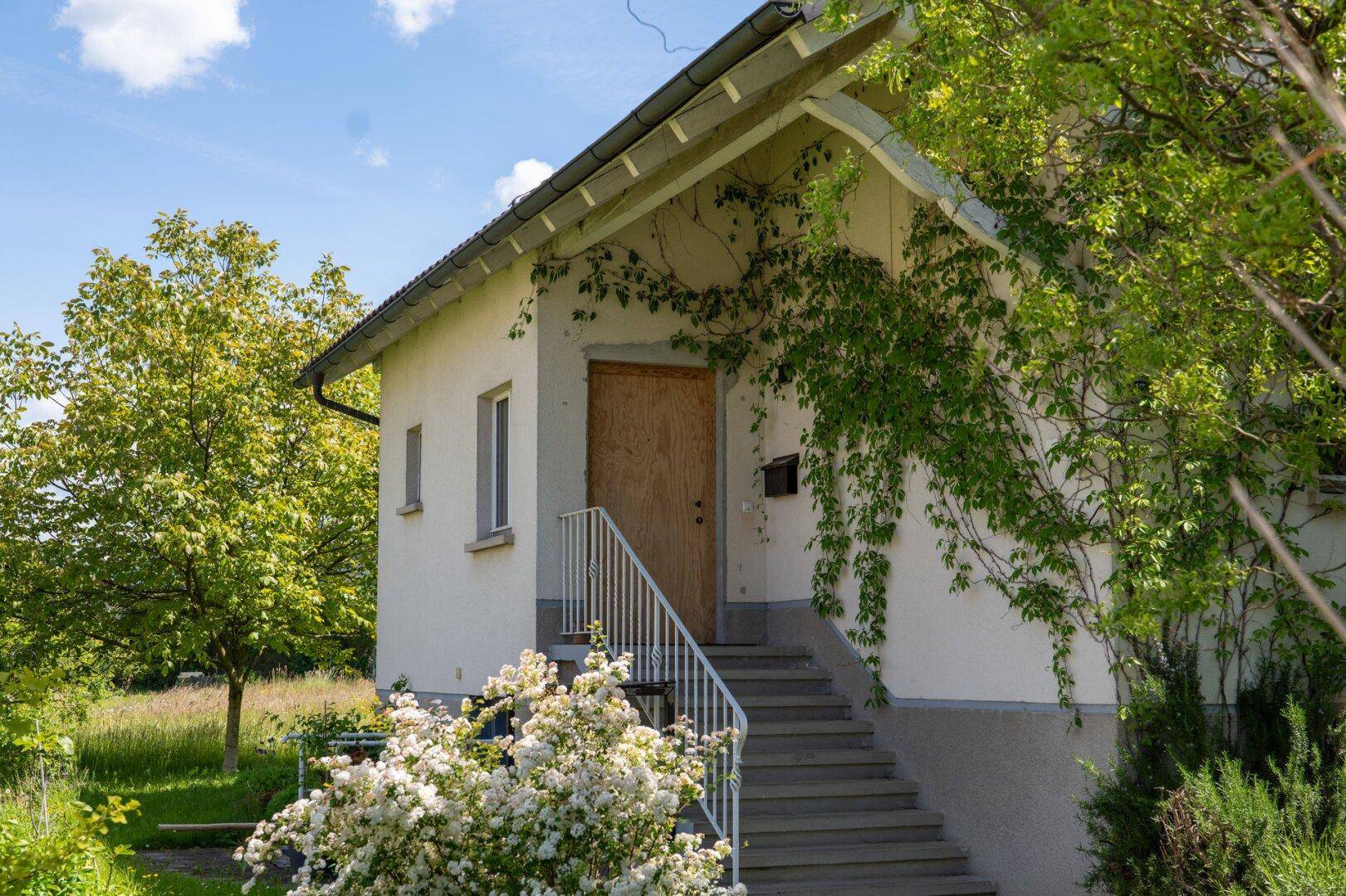 Eingangsbereich eines traditionellen Hauses mit Treppe und blühenden Sträuchern.