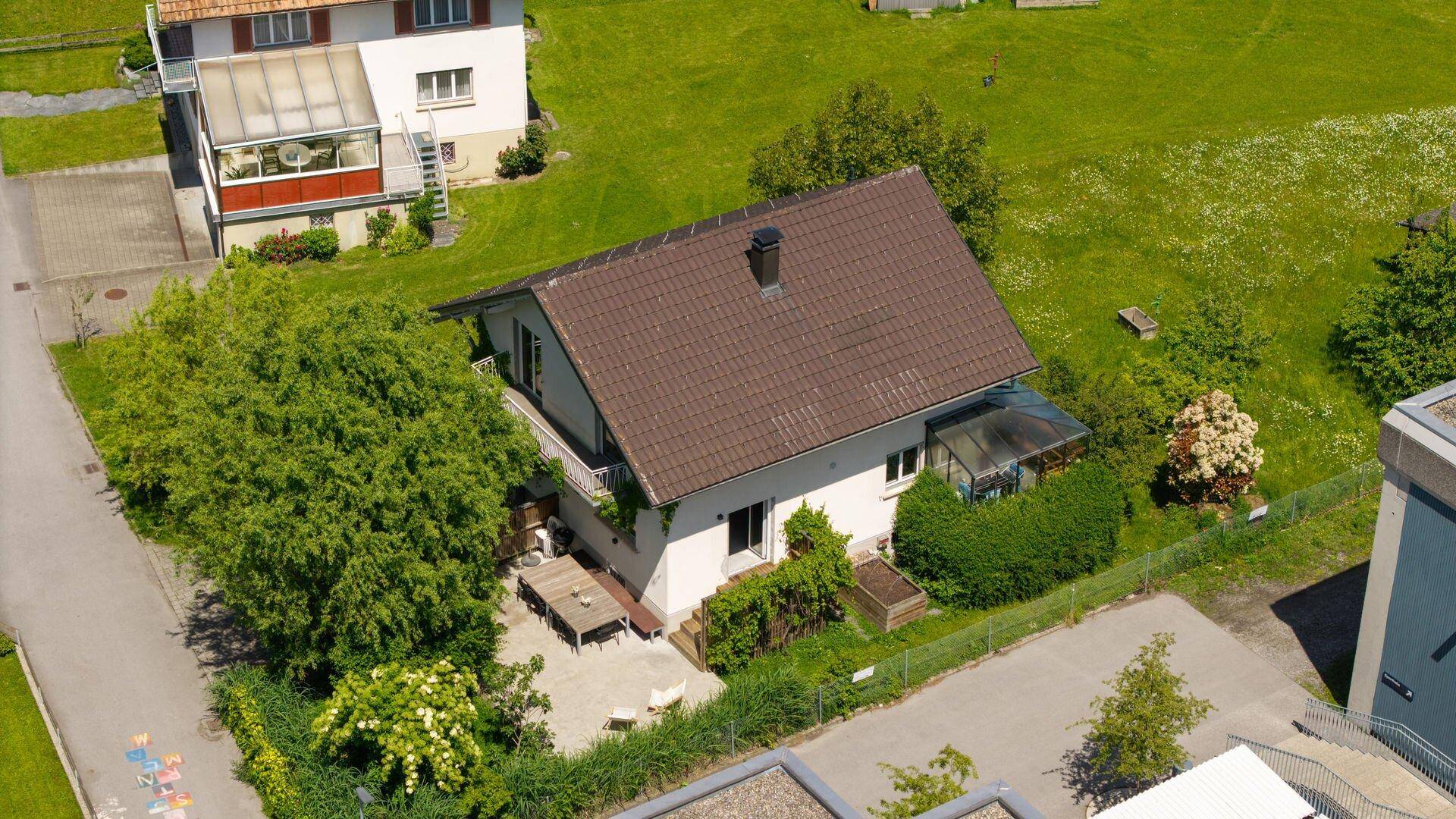 Luftaufnahme eines Hauses mit Garten, Terrasse und umliegender grüner Landschaft.
