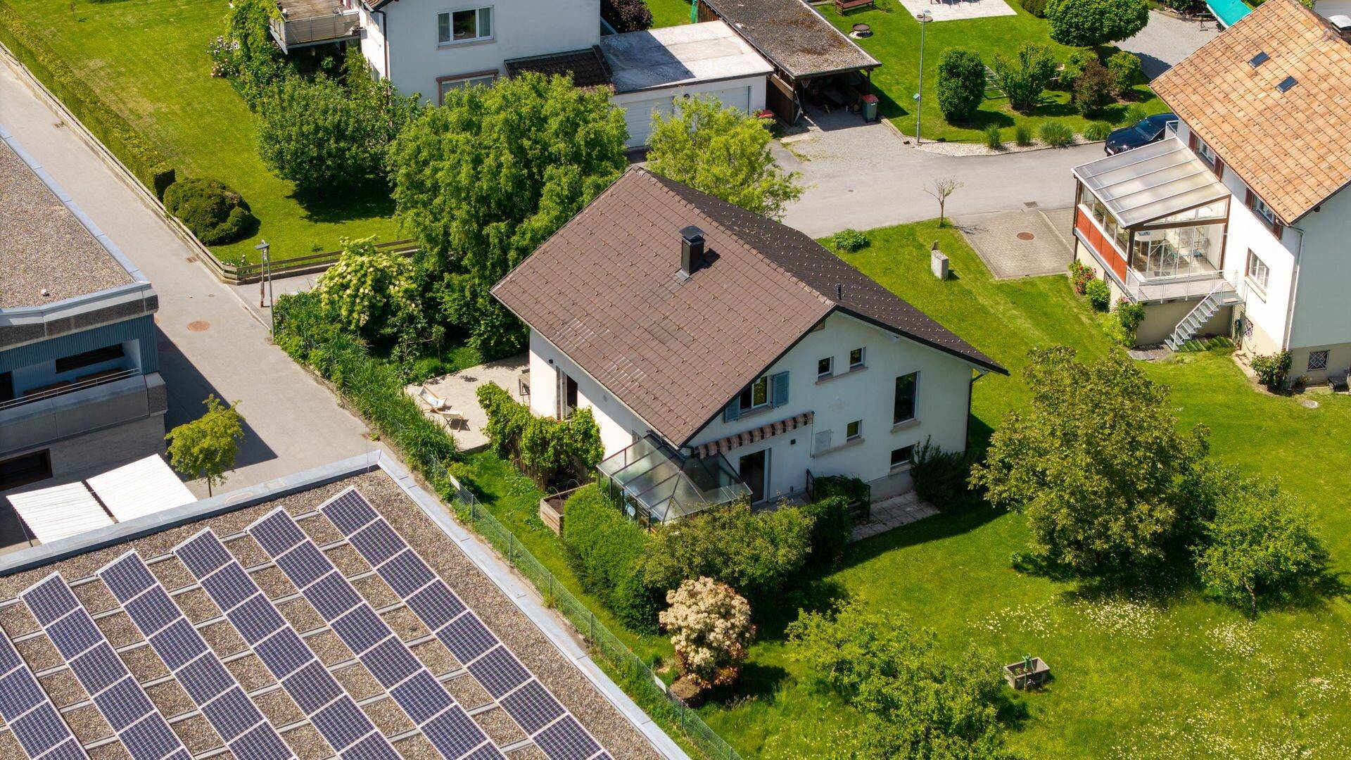 Luftaufnahme eines Hauses mit Garten, Solaranlage auf dem Nachbargebäude und viel Grün.