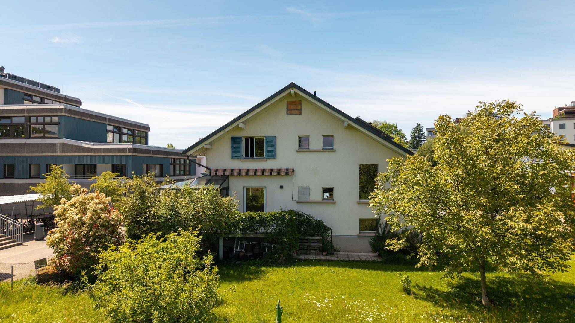 Freistehendes Einfamilienhaus mit Satteldach und großem Gartenbereich unter blauem Himmel.