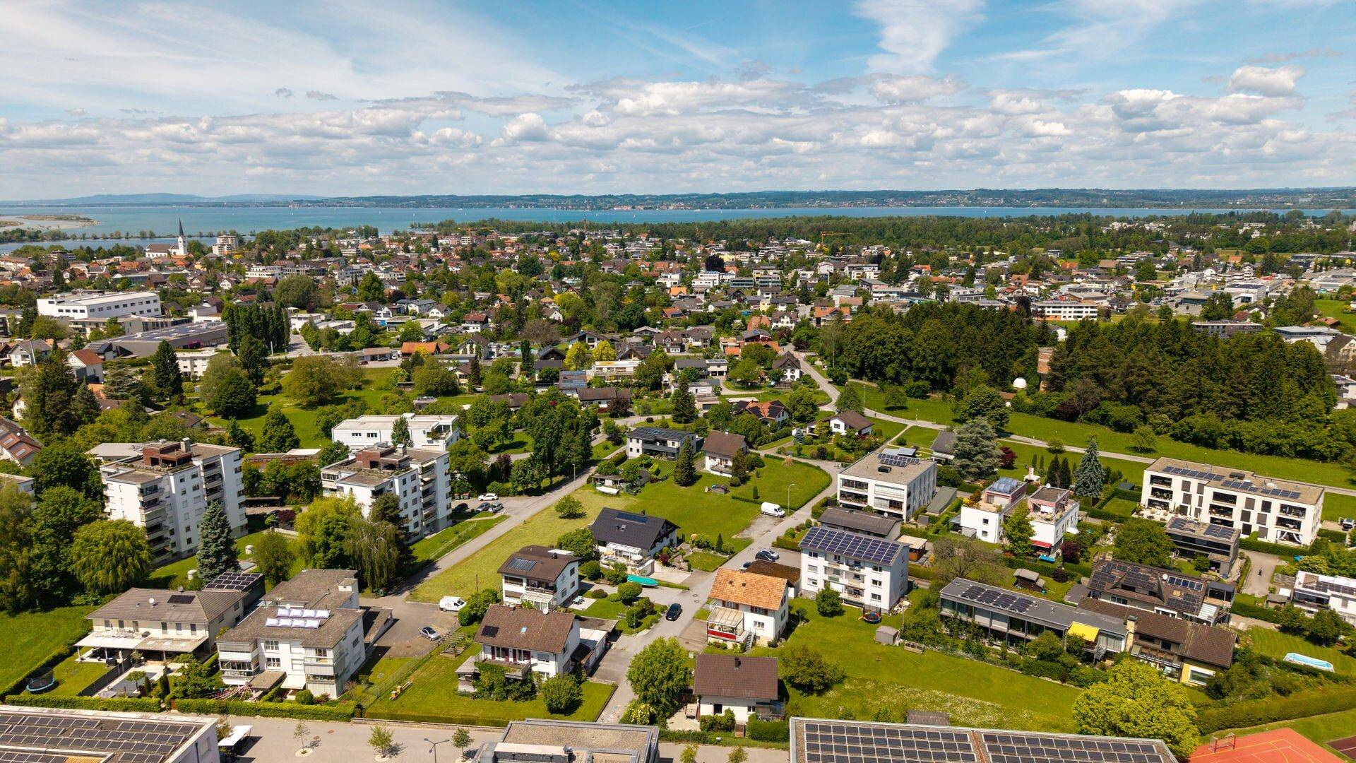 Panoramablick aus der Vogelperspektive über eine Stadt am See mit vielen Wohnhäusern und Grünflächen.