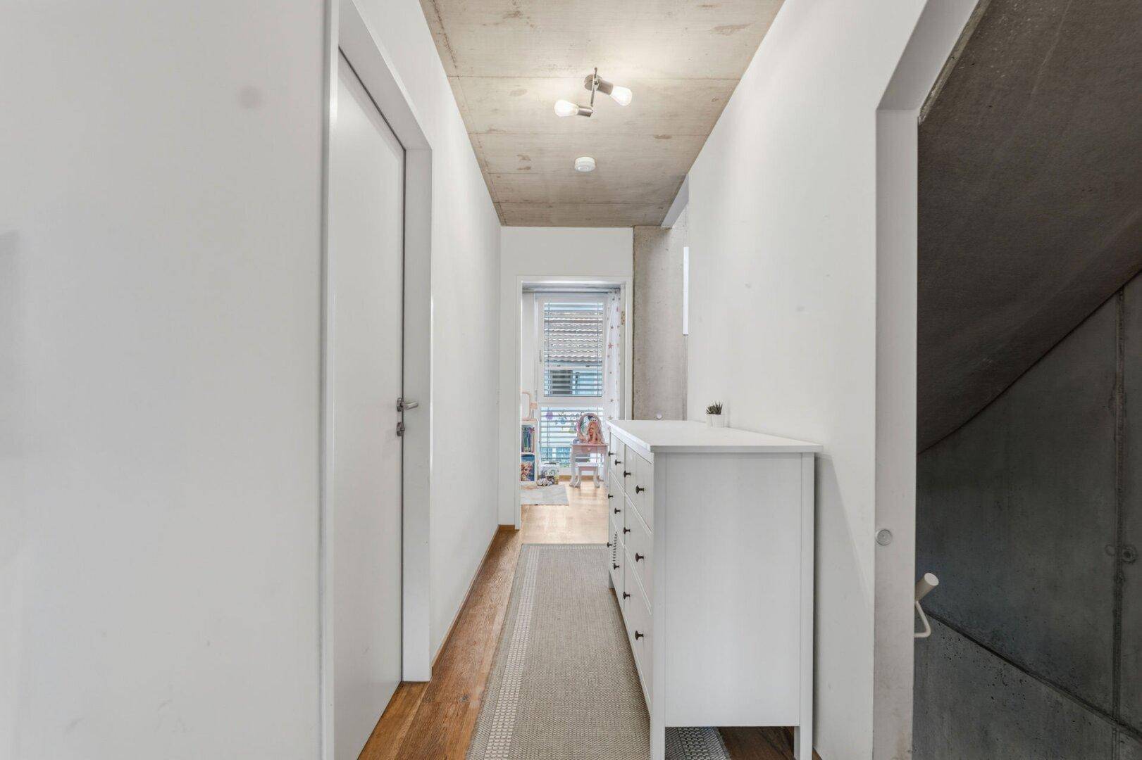 Heller Flur mit weißer Kommode und Holzboden, führt zu weiteren Räumen der Wohnung.