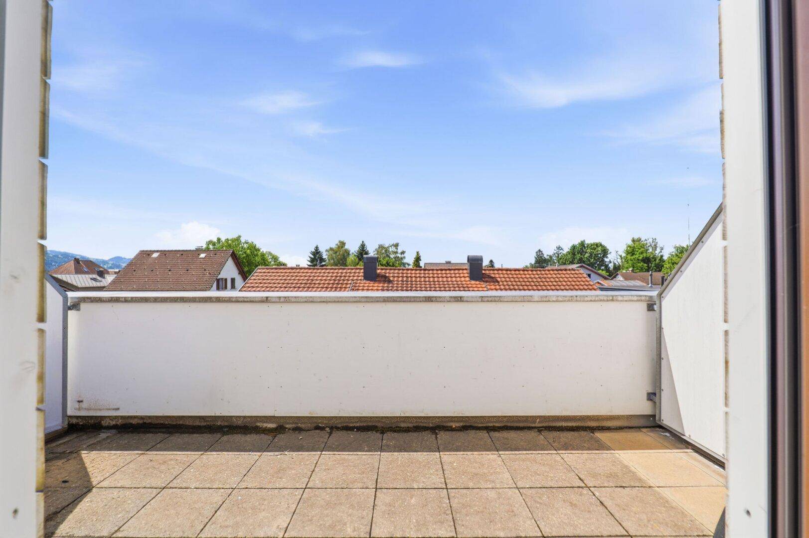 Geräumige Dachterrasse mit Fliesenboden und weitem Blick über die Dächer und Berge.