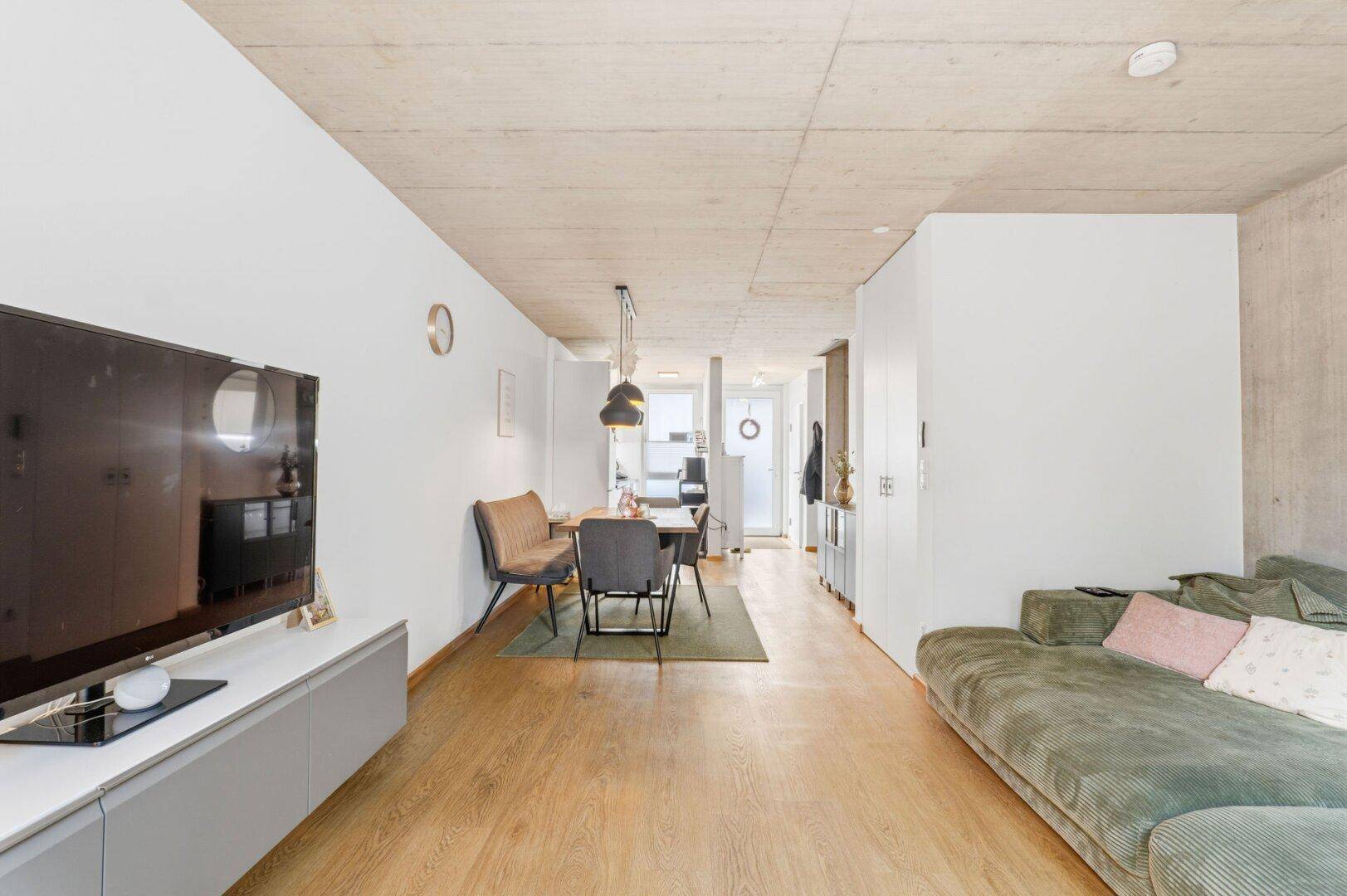 Gemütlicher Wohnbereich mit Sofa und Fernseher, offen zum Essbereich und Eingang.