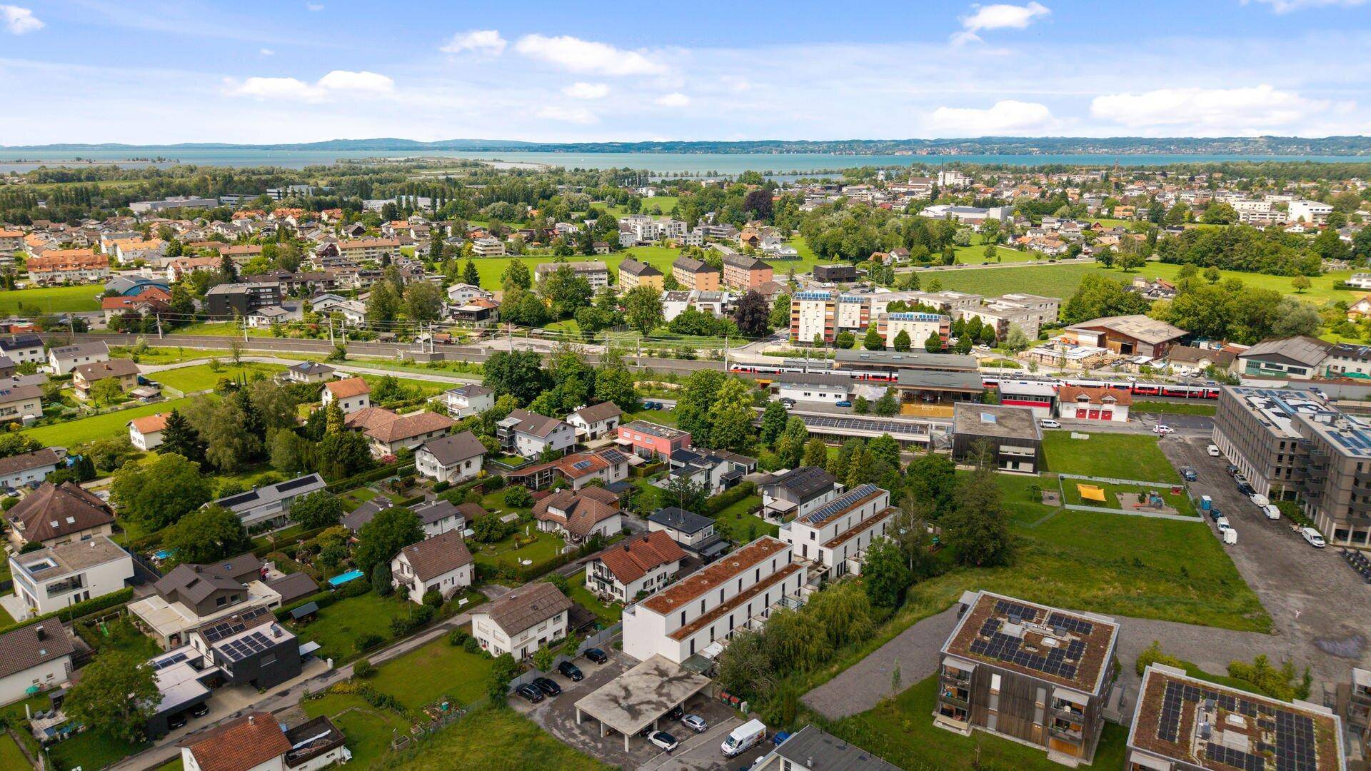 Panoramische Luftaufnahme einer Stadt mit See und Bergen im Hintergrund.