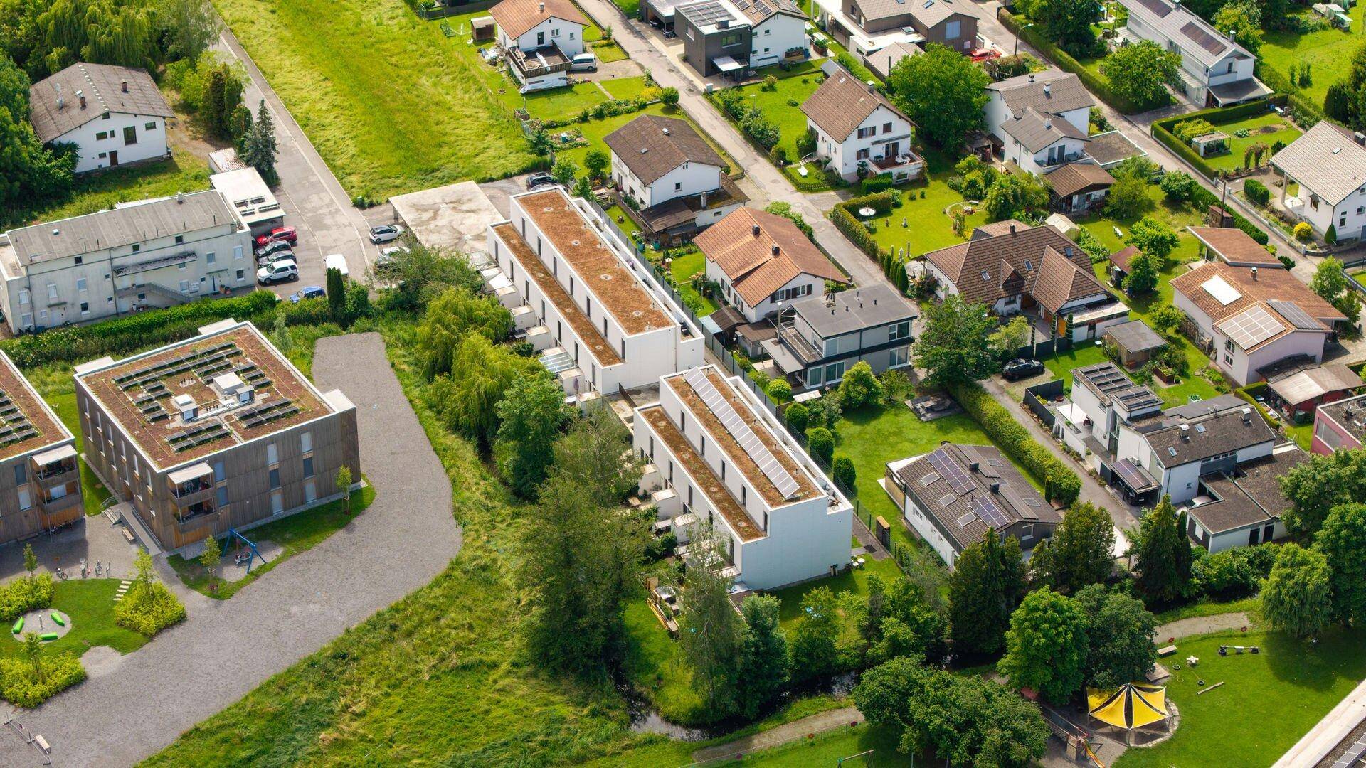 Luftaufnahme von modernen Wohngebäuden und Einfamilienhäusern in einer grünen Landschaft.