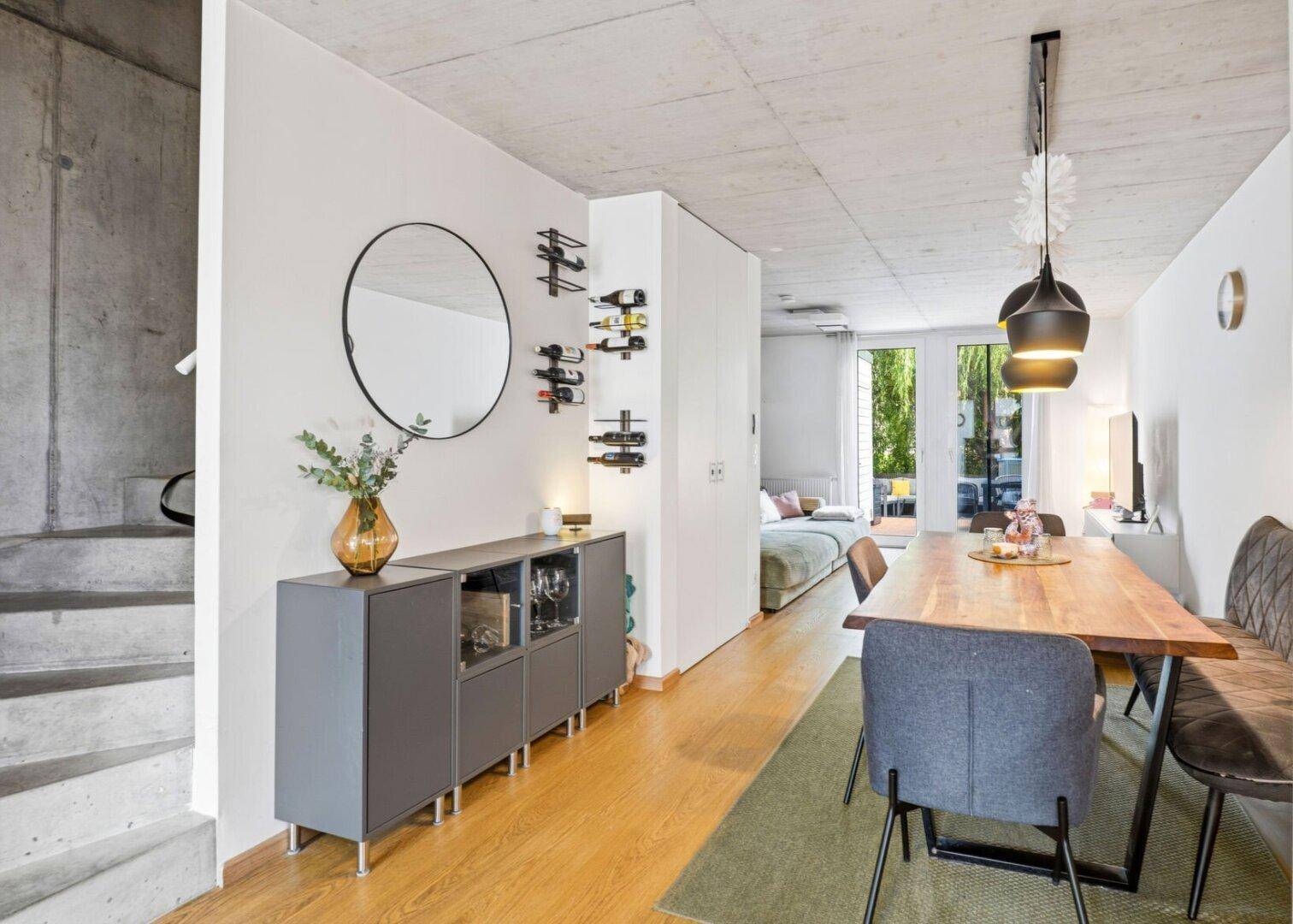 Essbereich mit Sideboard, Spiegel und Weinflaschenregal, angrenzend an Betontreppe.