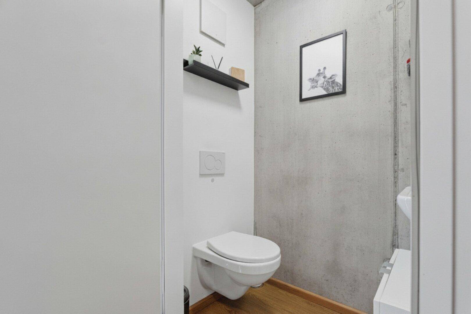 Modernes Gäste-WC mit wandhängender Toilette und einer Akzentwand aus Beton.