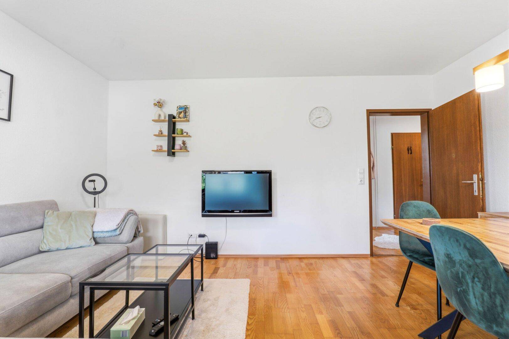 Wohnzimmer mit Sofa, Fernseher und Holzboden, verbunden mit dem Essbereich.