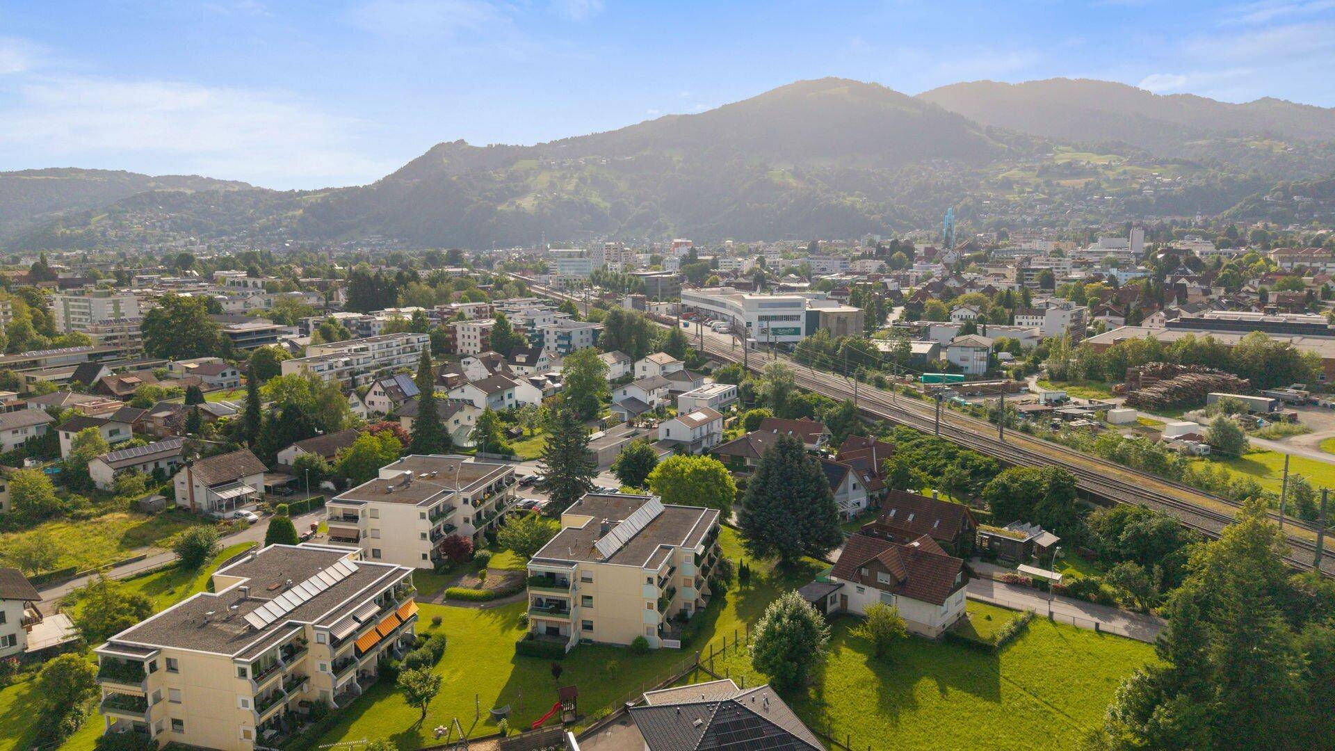 Weitläufige Luftaufnahme einer Stadtlandschaft mit Wohngebäuden, Bergen und Infrastruktur.
