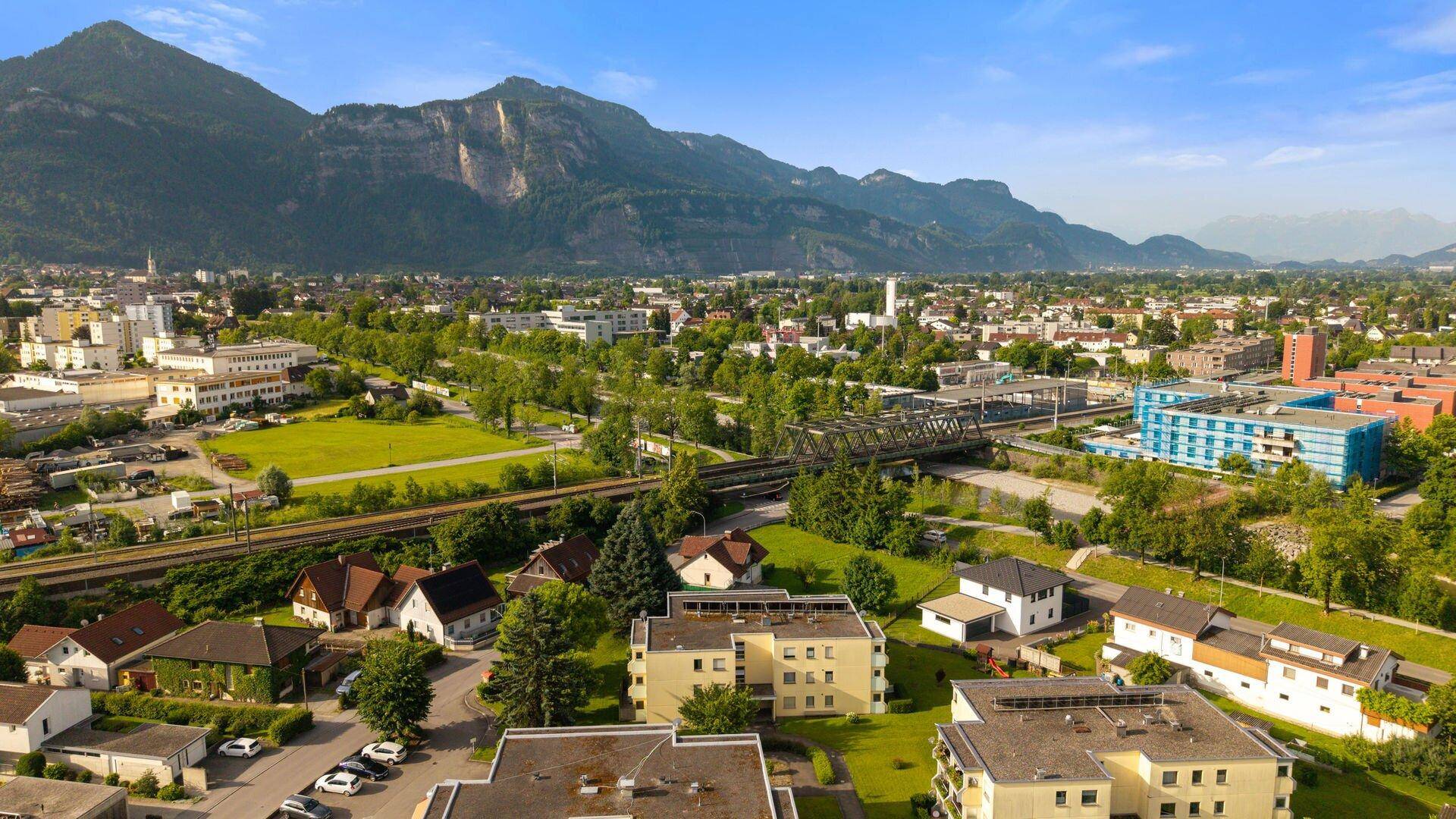 Panoramablick auf eine Stadt mit Bergen, Wohngebäuden und einer Eisenbahnbrücke.