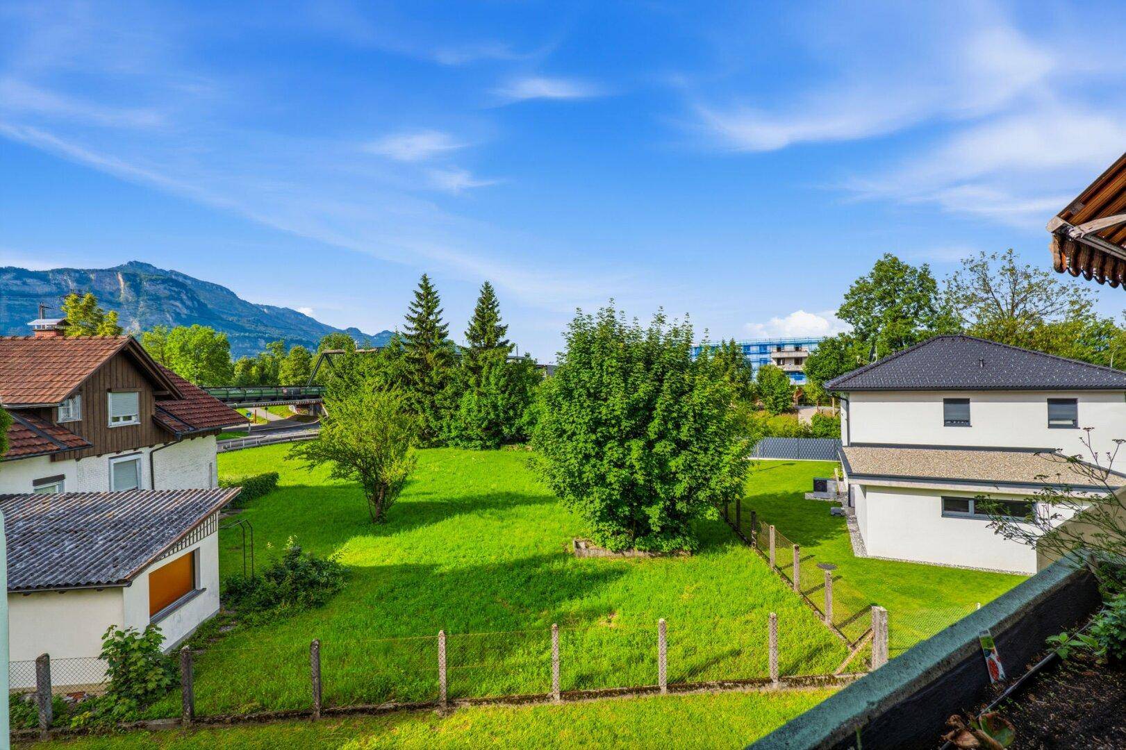 Weitläufige Grünfläche mit Bäumen und Bergen im Hintergrund, umgeben von Wohnhäusern.