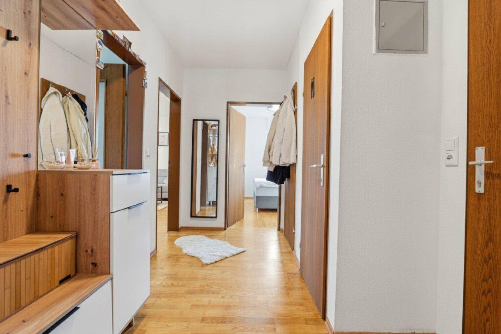 Geräumiger Flur mit Holzboden, Garderobe und Spiegel, der zu den Zimmern führt.