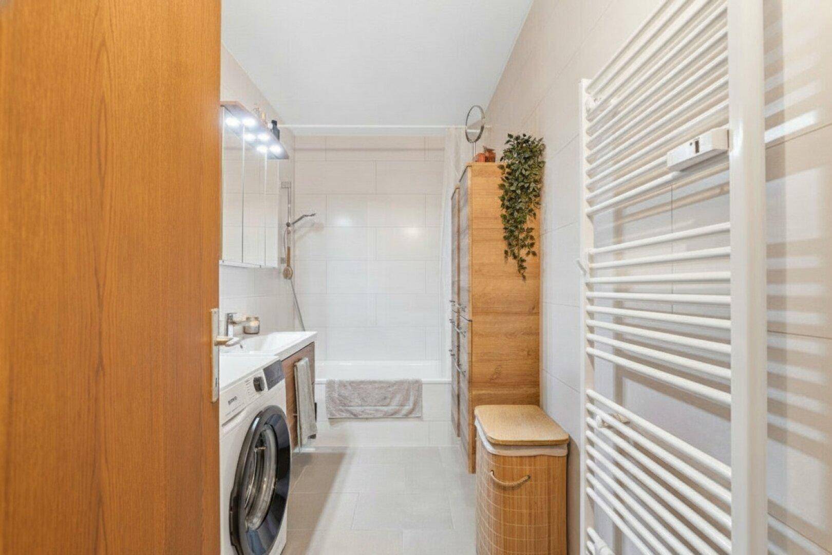 Modernes Badezimmer mit Badewanne, Waschmaschine und beheiztem Handtuchhalter.