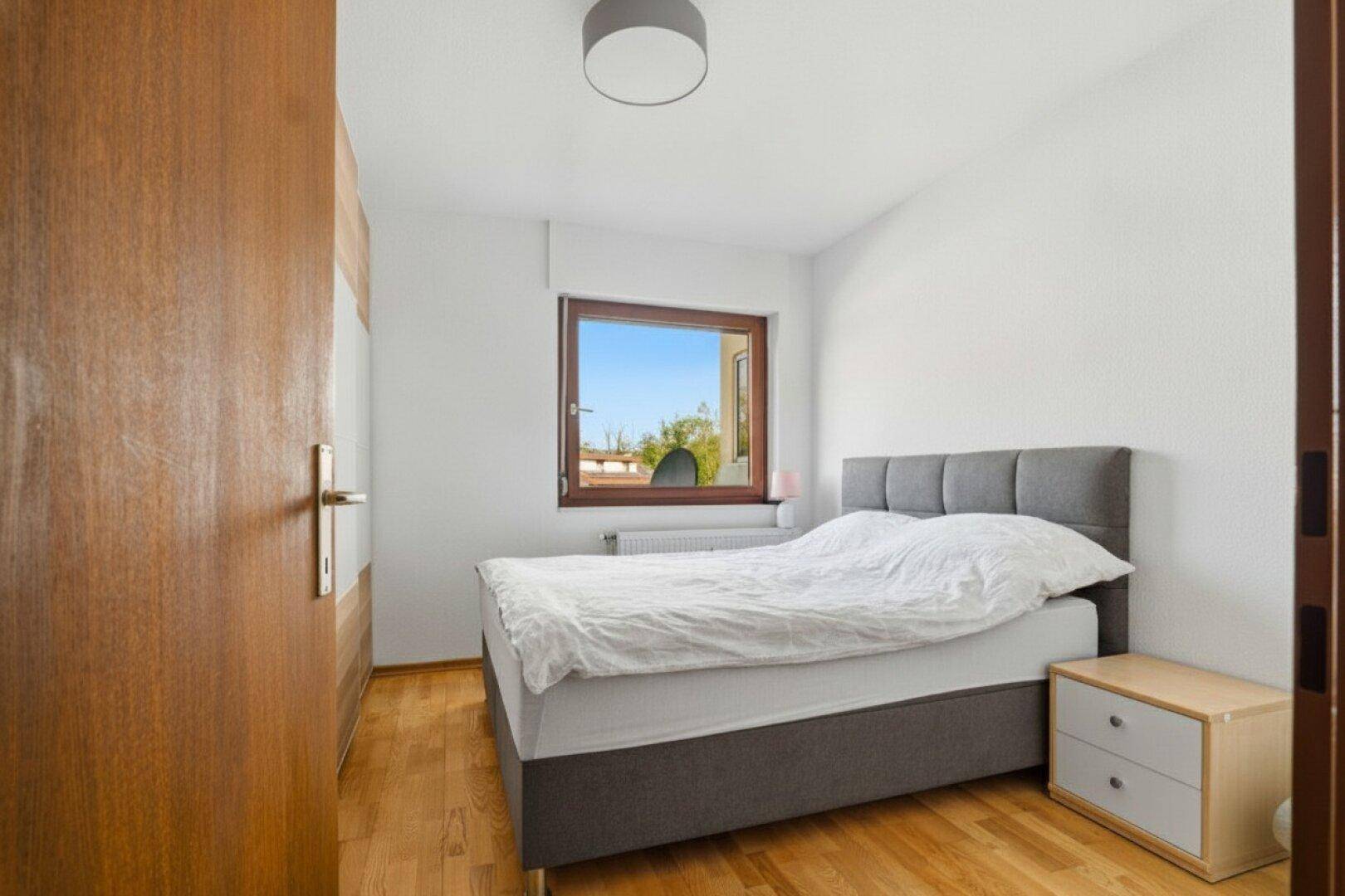 Helles Schlafzimmer mit Holzboden, Doppelbett und Fenster mit Blick nach draußen.
