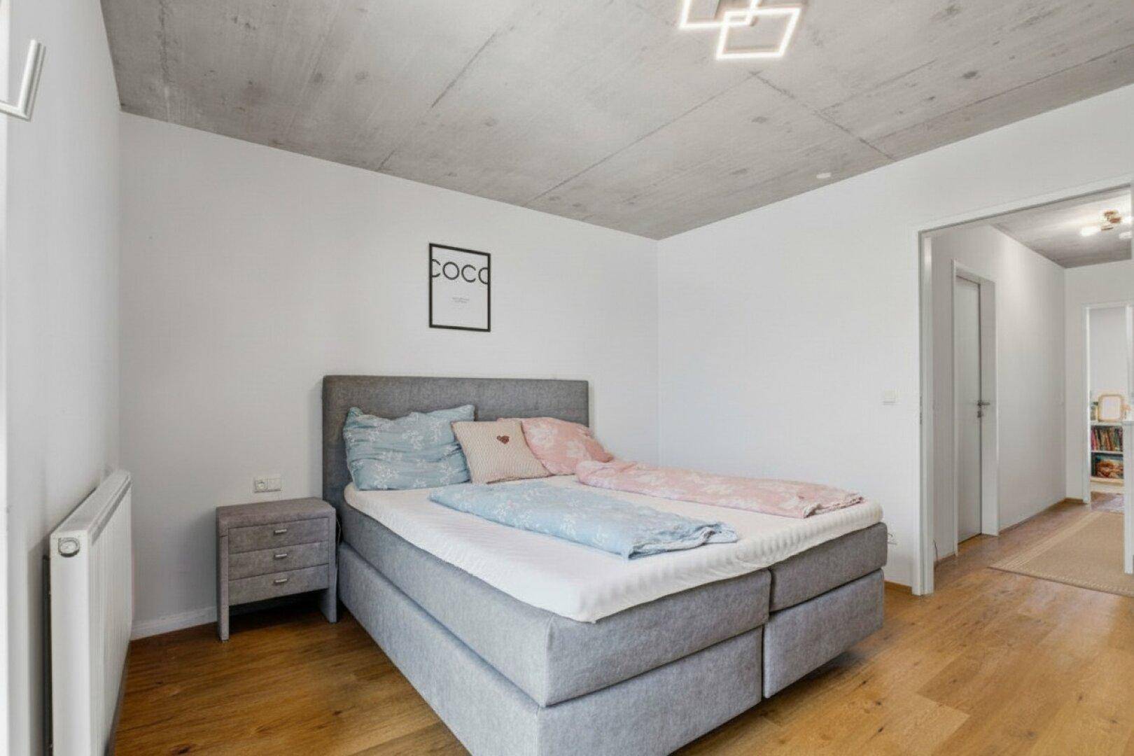 Modernes Schlafzimmer mit Doppelbett und Zugang zum Flur, helle Wände und Holzboden.