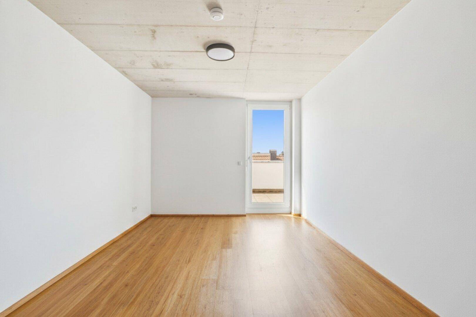 Leerer Raum mit Holzboden und Zugang zu einem Außenbereich, ideal für individuelle Gestaltung.