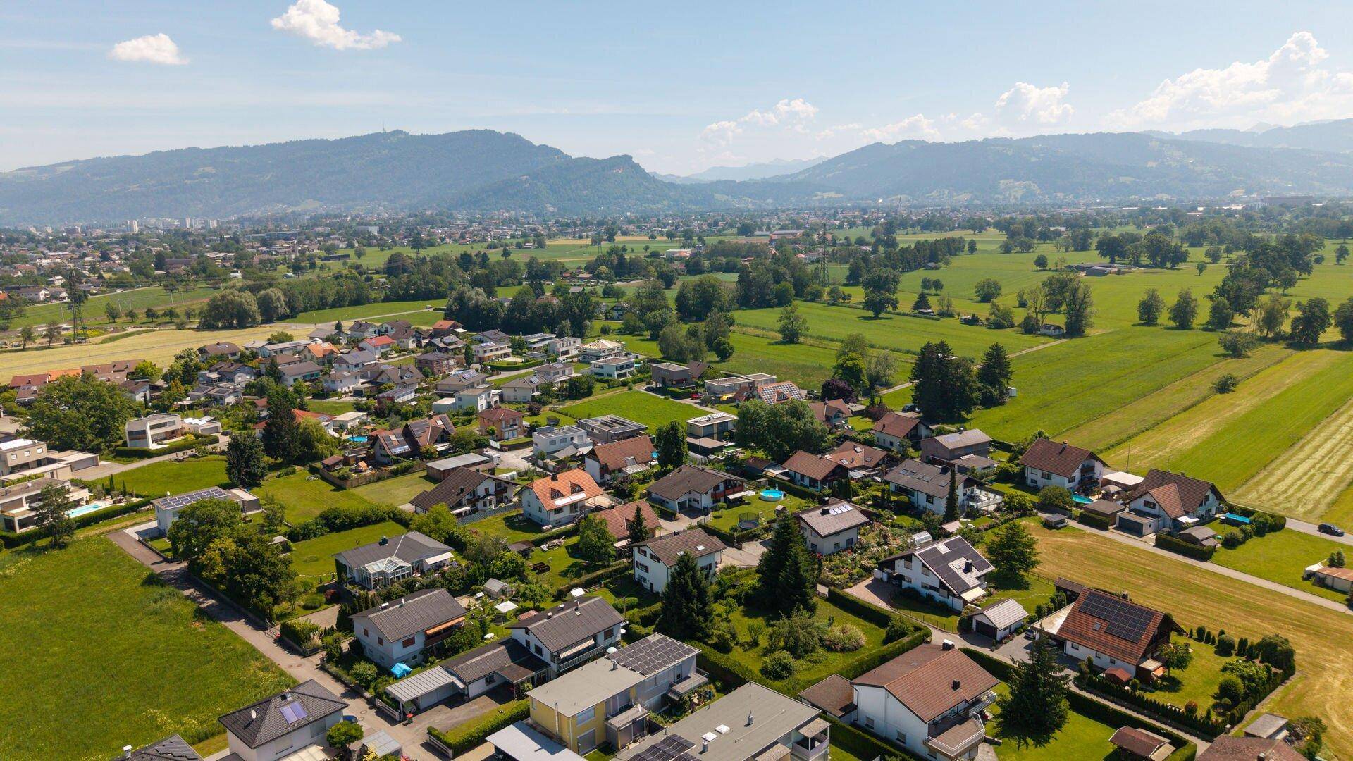 Luftaufnahme einer Wohngegend mit weitläufigen Grünflächen und einer malerischen Bergkulisse.