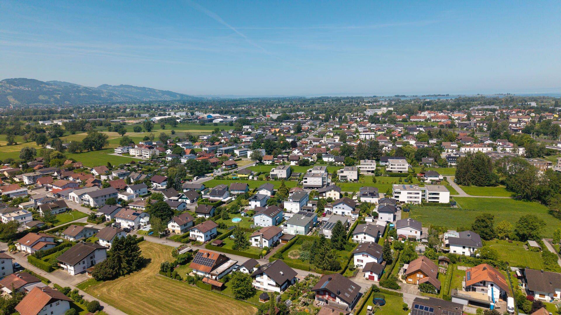 Panoramische Luftaufnahme einer Wohnsiedlung mit grüner Umgebung und Bergen am Horizont.