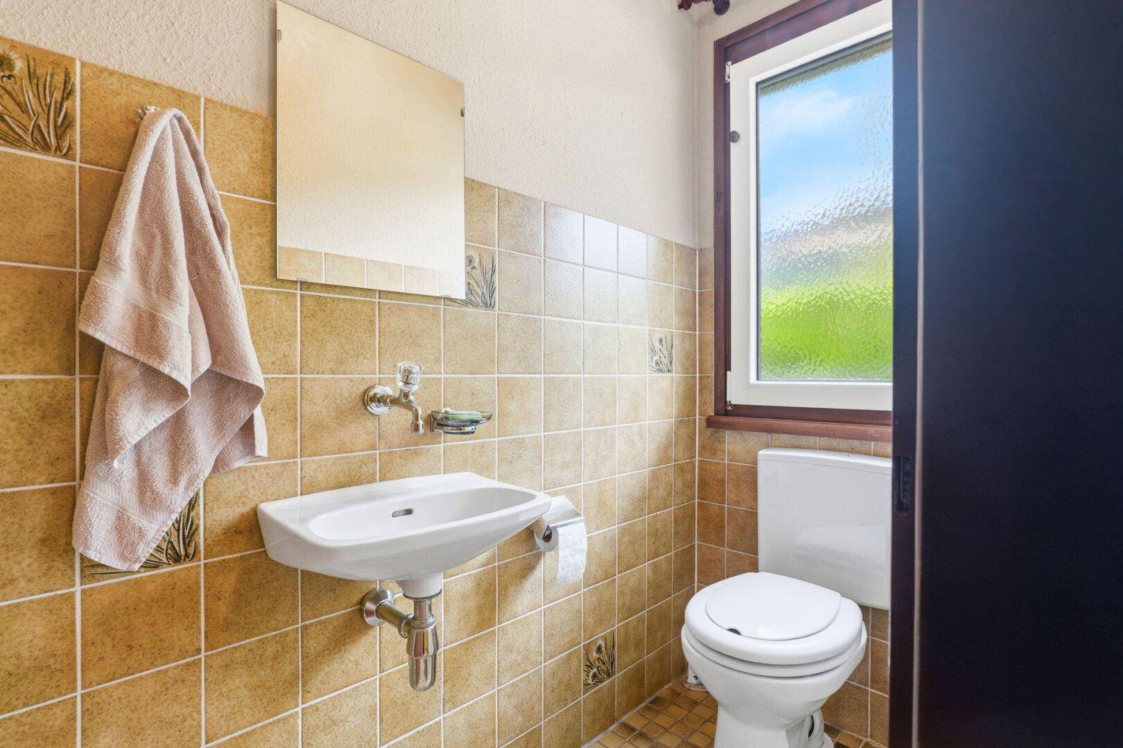 Kleines Gäste-WC mit beigefarbenen Fliesen, Waschbecken und Fenster.