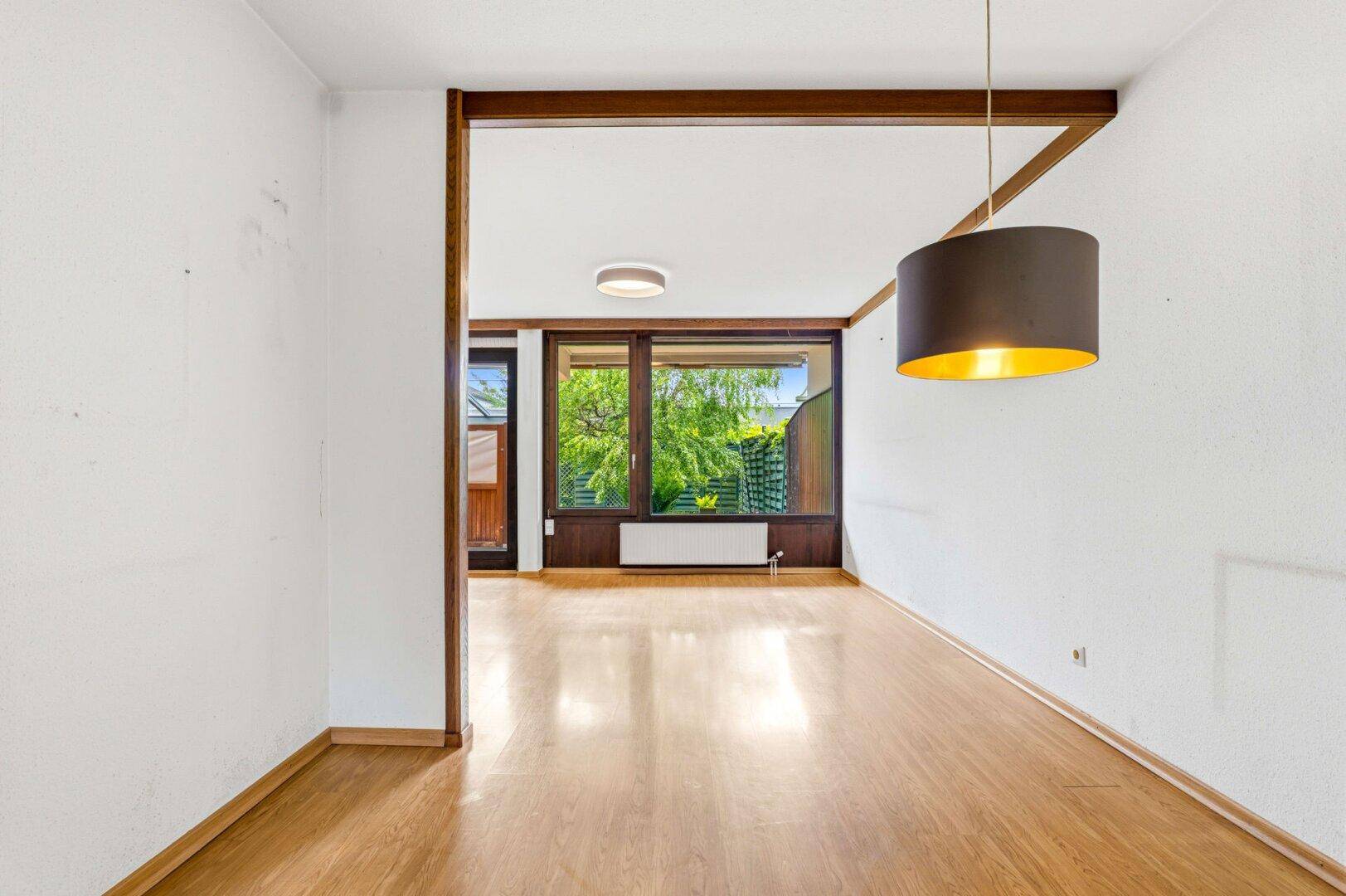 Heller Raum mit Parkettboden, Holzbalken und großem Fenster mit Blick ins Grüne.