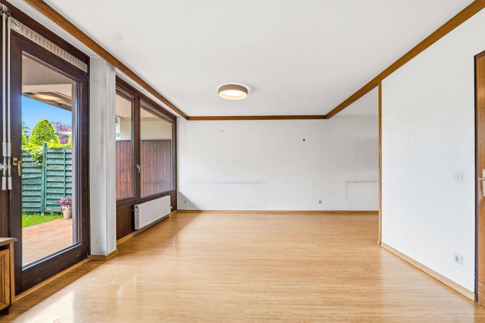 Geräumiges Wohnzimmer mit Parkettboden und Zugang zum Garten durch große Glastüren.