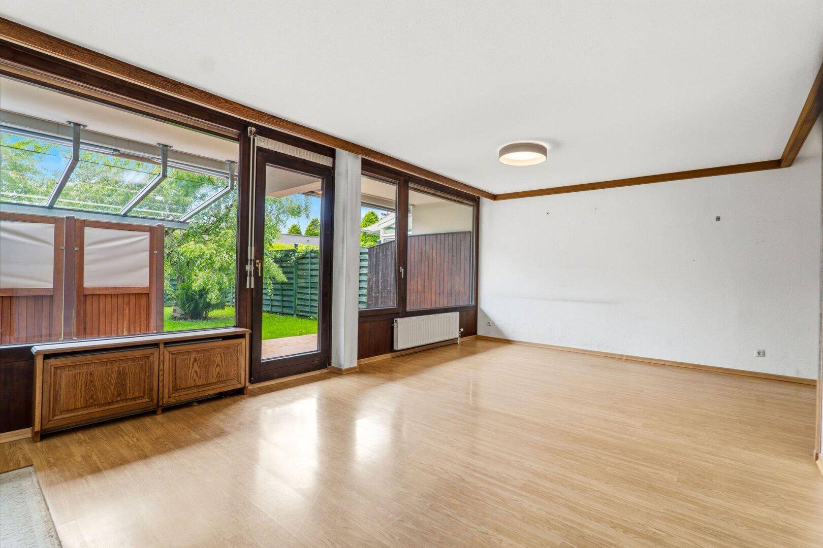 Heller Wohnraum mit Parkettboden und breiten Fenstern mit Blick auf den Garten.