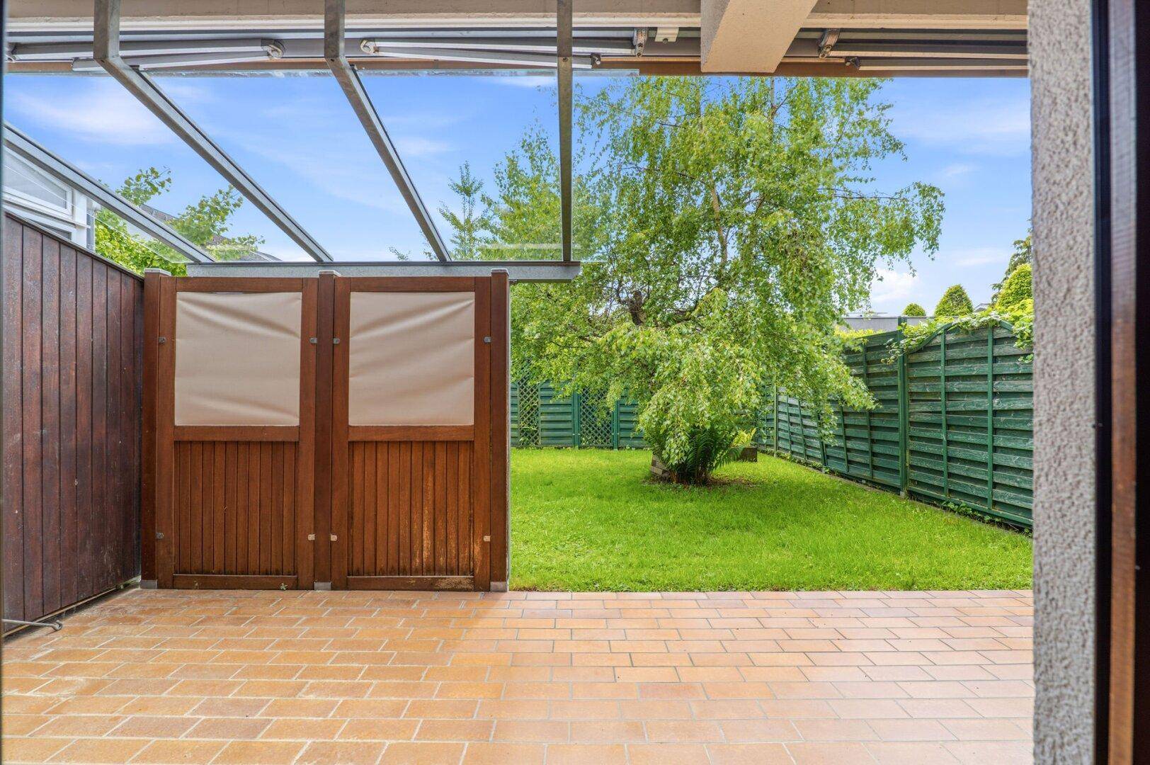Gepflasterte Terrasse mit Blick auf den grünen Garten und hohe Hecken.
