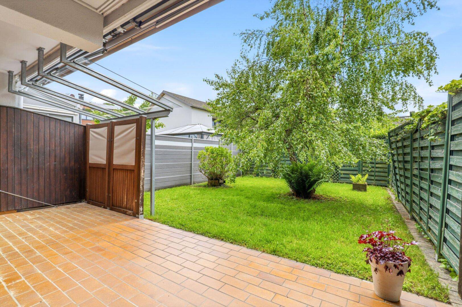 Sonniger Terrassenbereich mit Sitzgelegenheiten und Blick auf den gepflegten Garten.