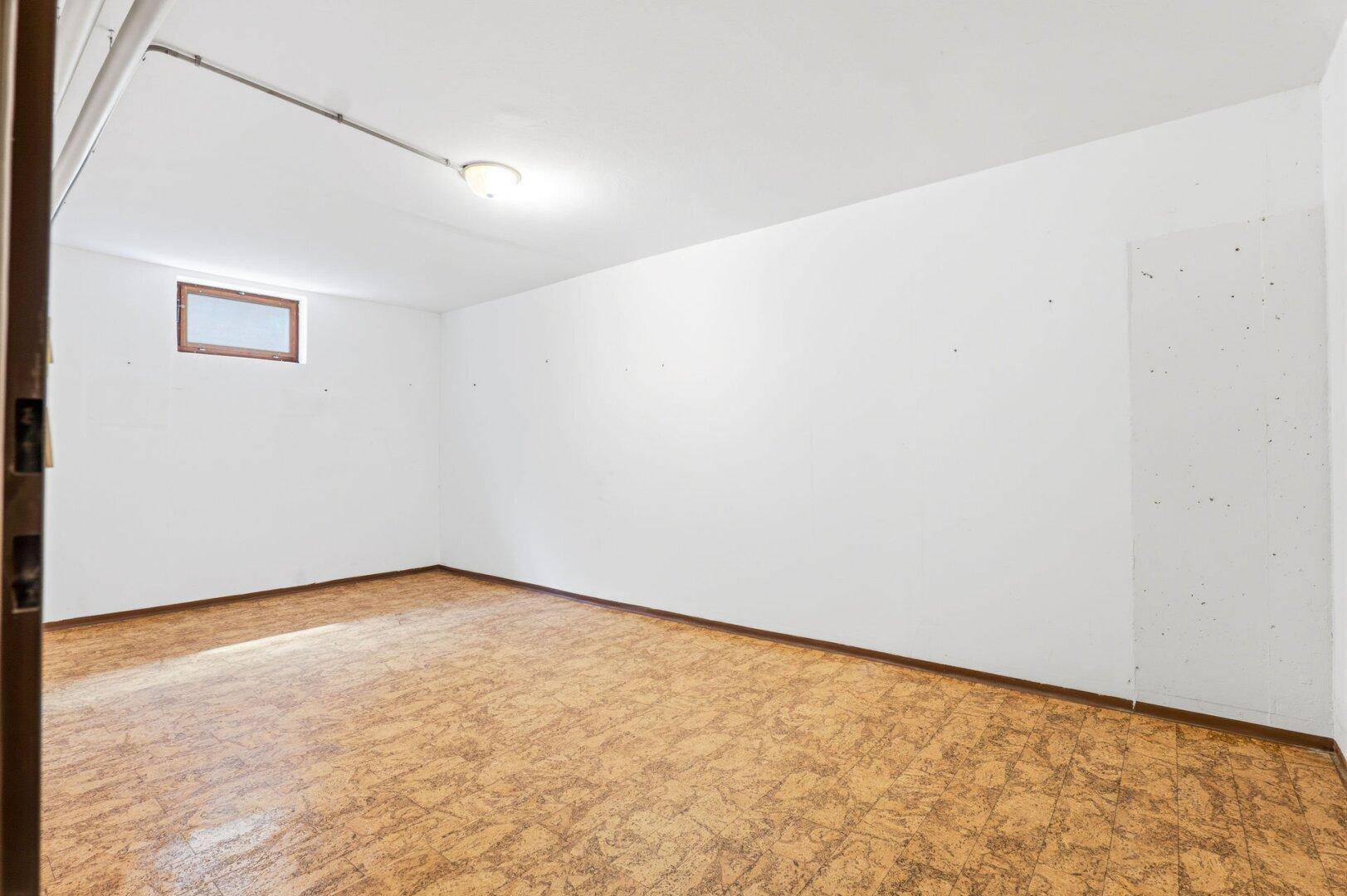 Heller Kellerraum mit weiß gestrichenen Wänden und kleinem Fenster, ideal als Abstellraum.