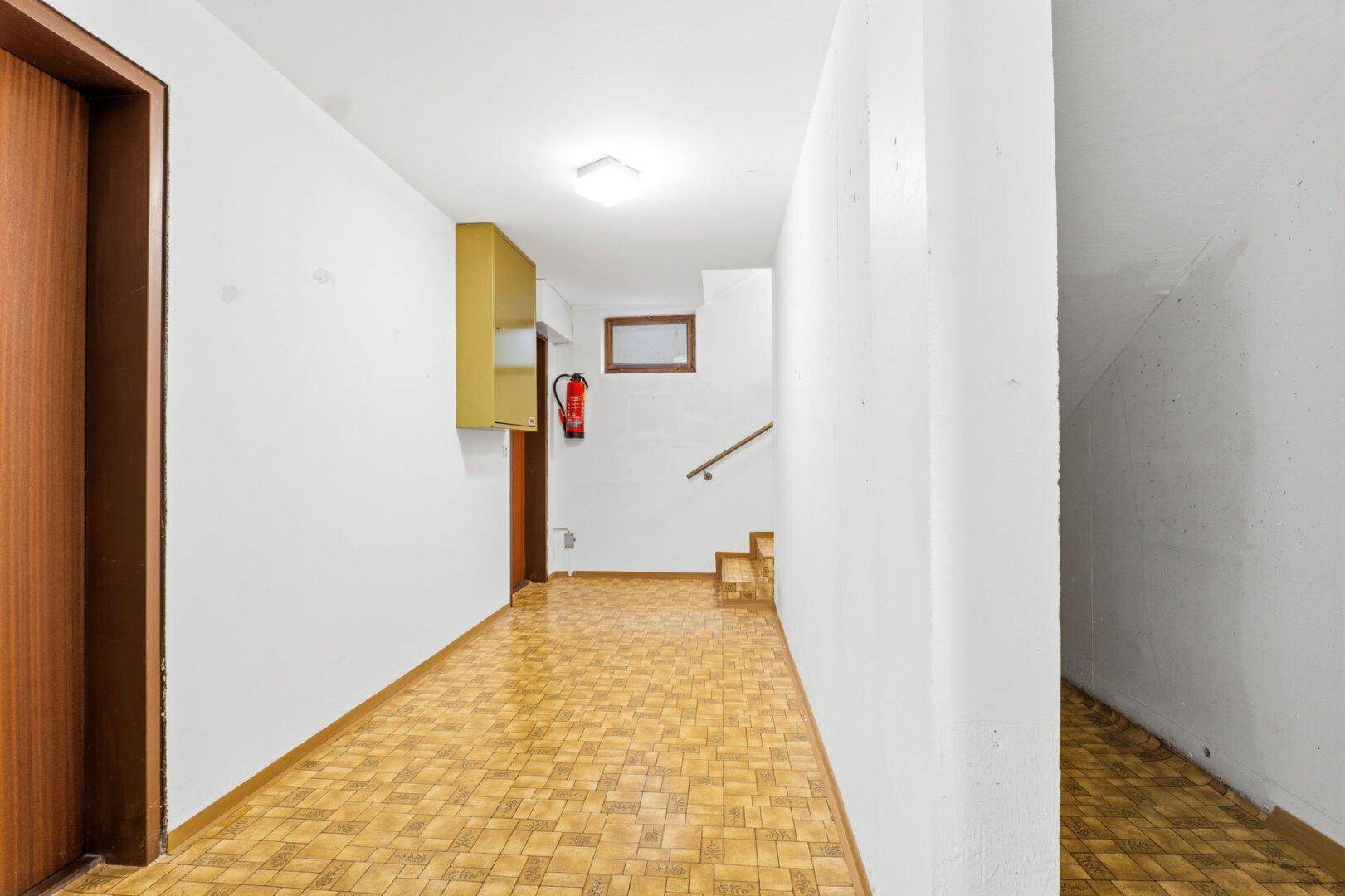 Kellerflur mit PVC-Boden, weiß gestrichenen Wänden und Treppenaufgang.