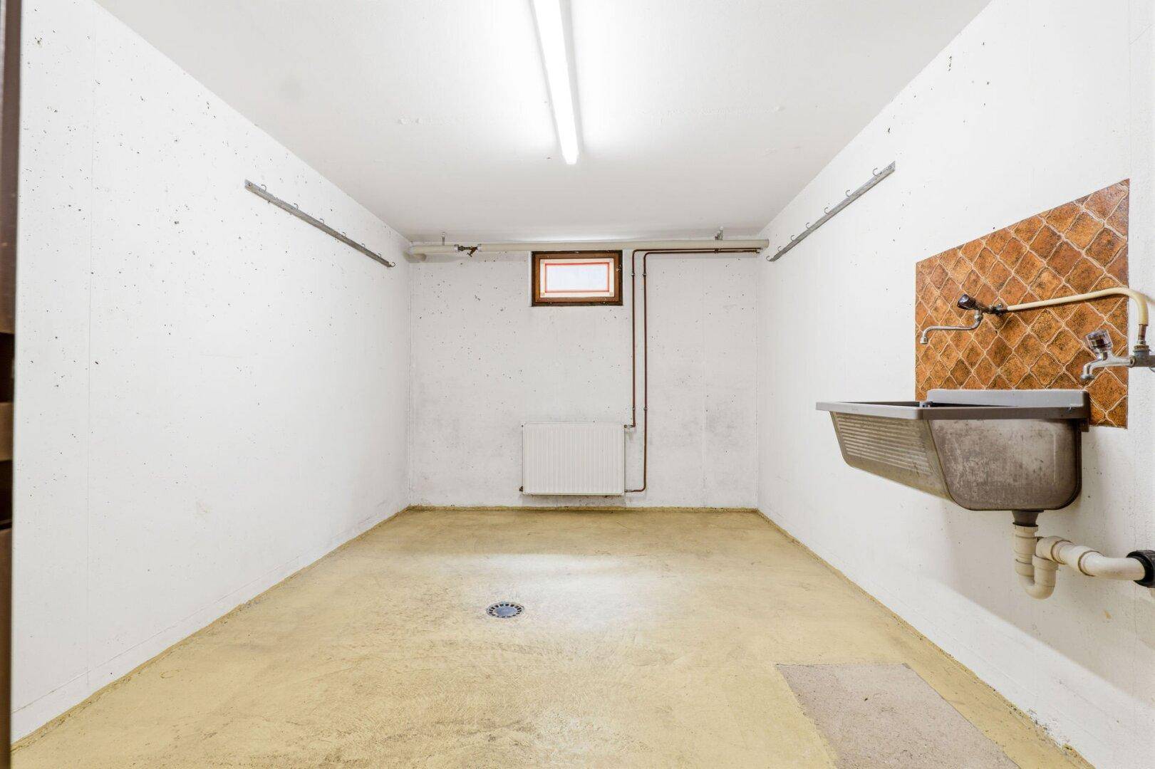 Funktionaler Kellerraum mit Waschbecken, Heizkörper und kleinem Fenster für vielseitige Nutzung.