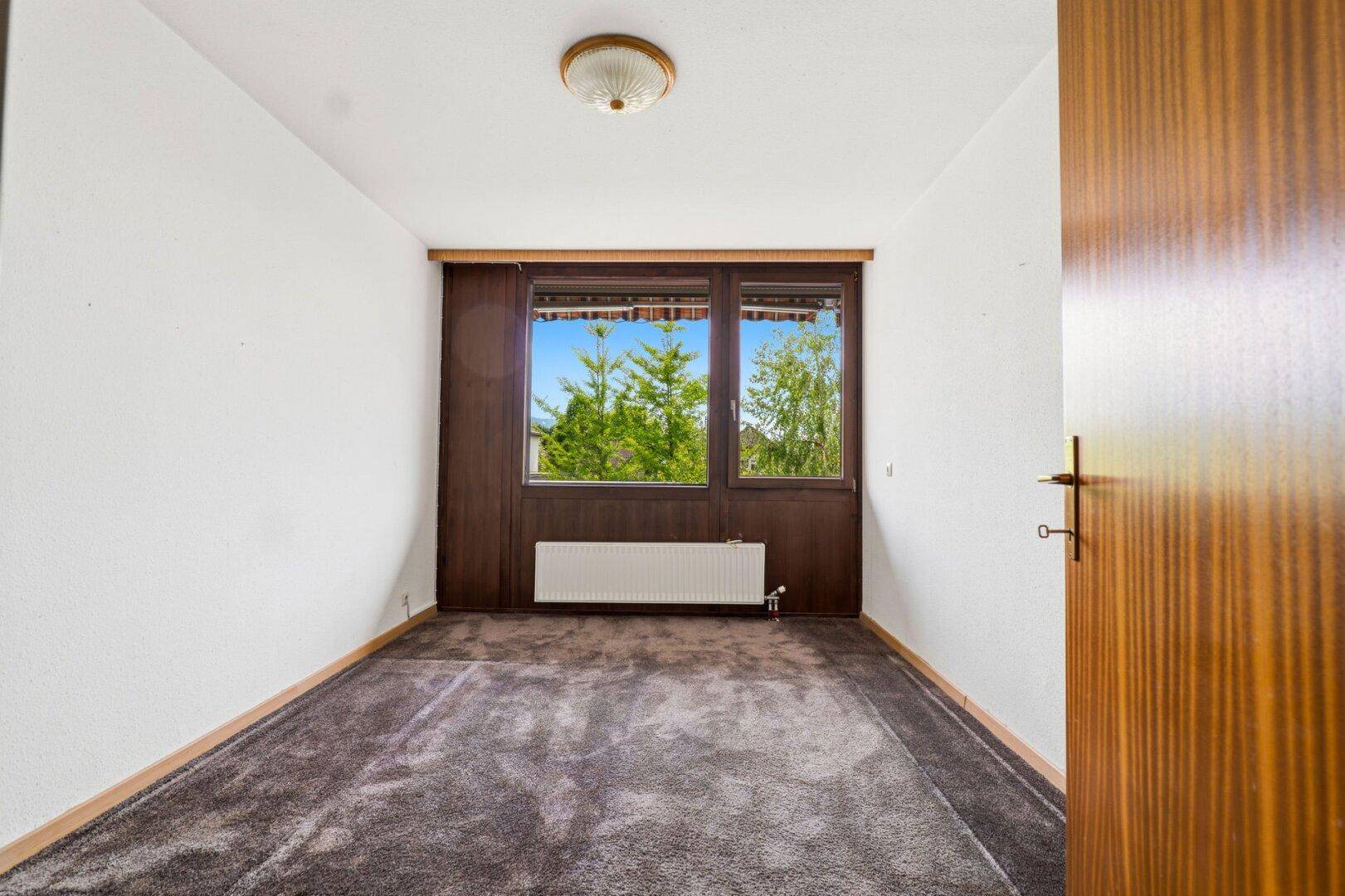 Schlafzimmer mit Teppichboden, großen Fenstern und Blick ins Grüne.