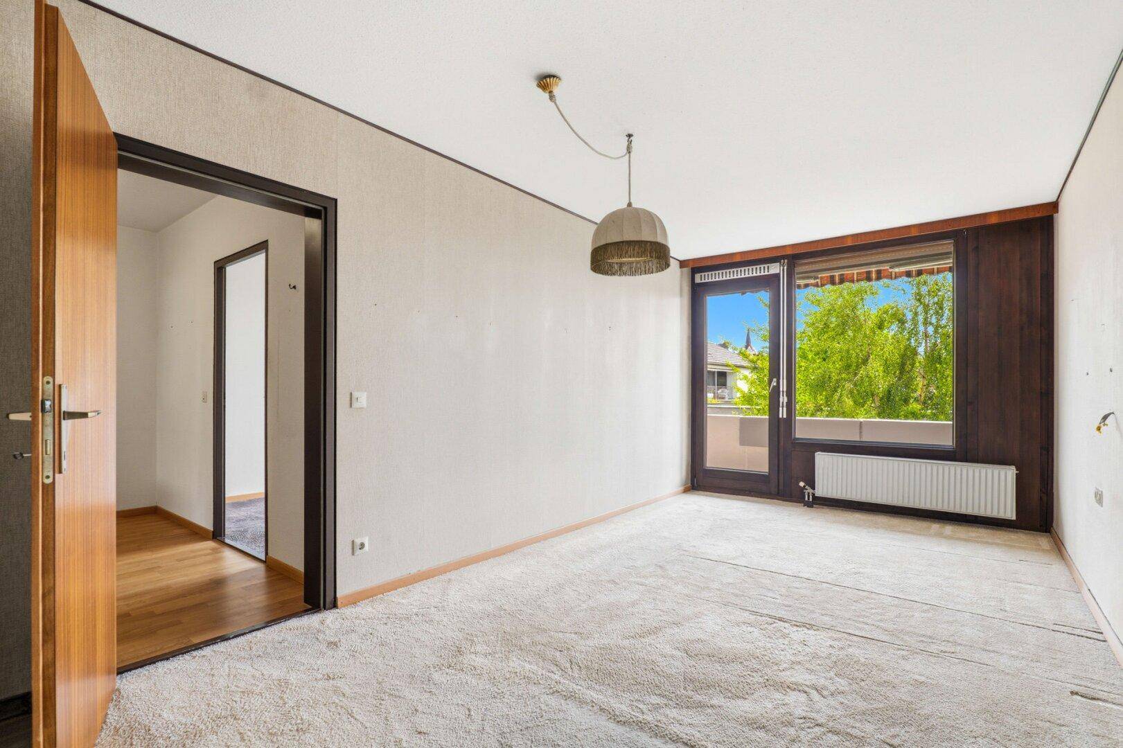 Schlafzimmer mit Teppichboden, Balkonzugang und Blick auf die Umgebung.