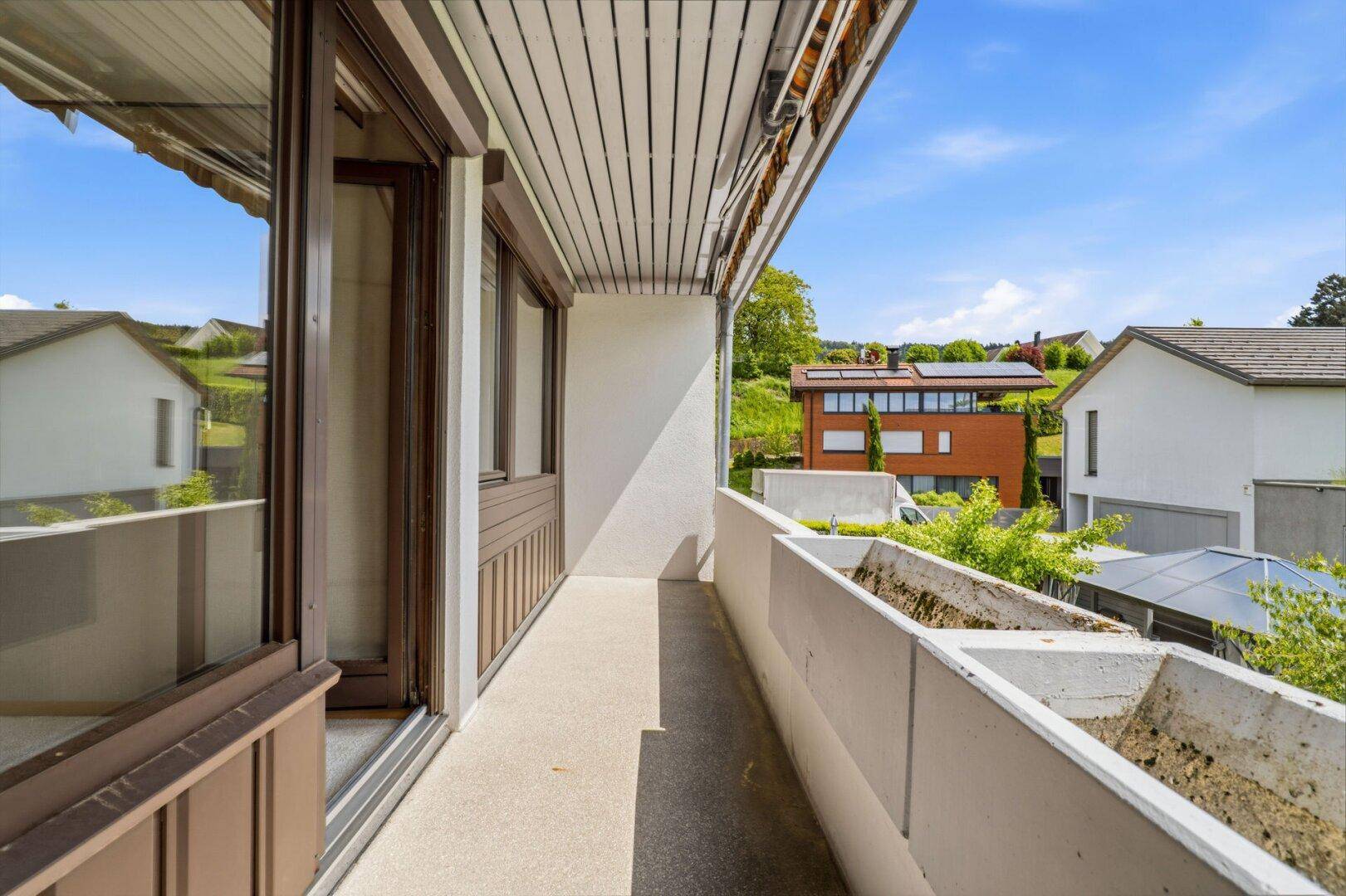 Langer Balkon mit Betonbrüstung und Blick auf die umliegenden Häuser und Landschaft.