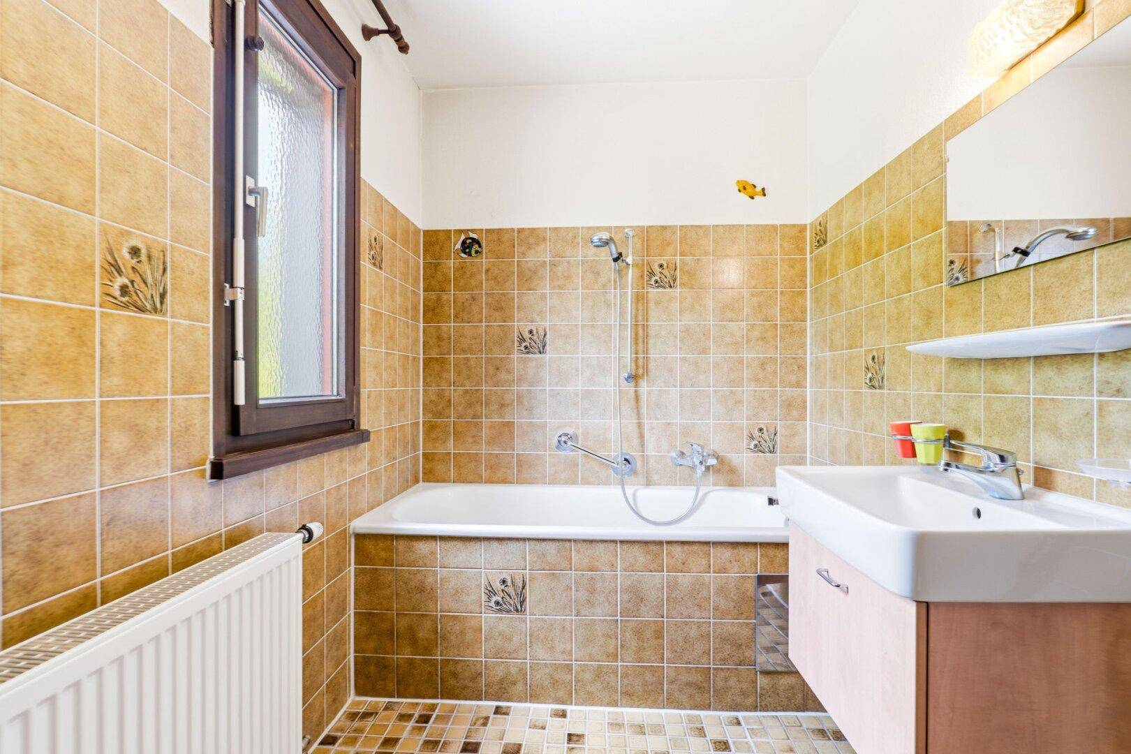 Badezimmer mit Badewanne, Waschbecken, Spiegel und beigefarbenen Fliesen.