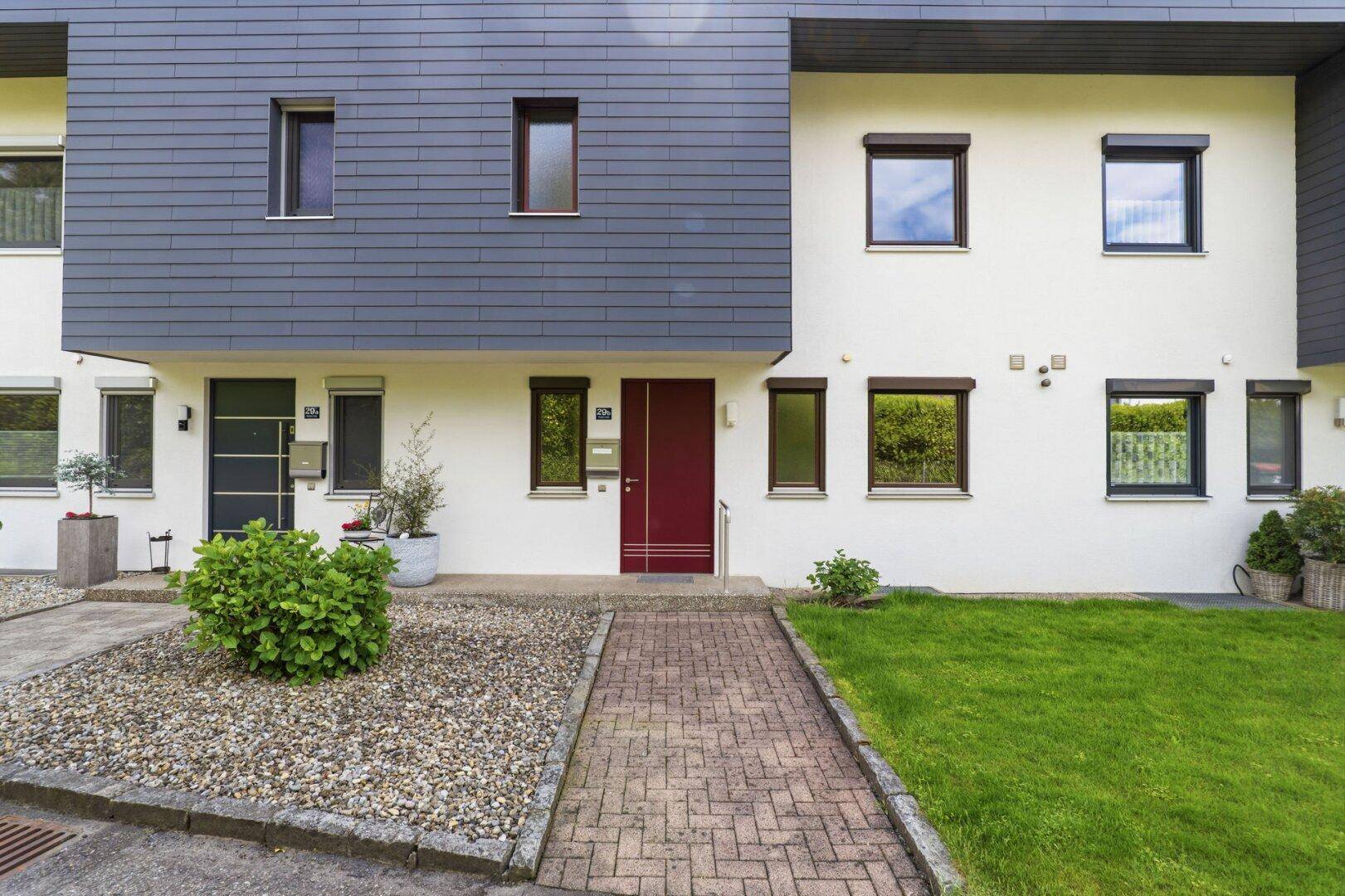 Moderne Reihenhausfassade mit roter Eingangstür, dunkler Verkleidung und gepflegtem Vorgarten.