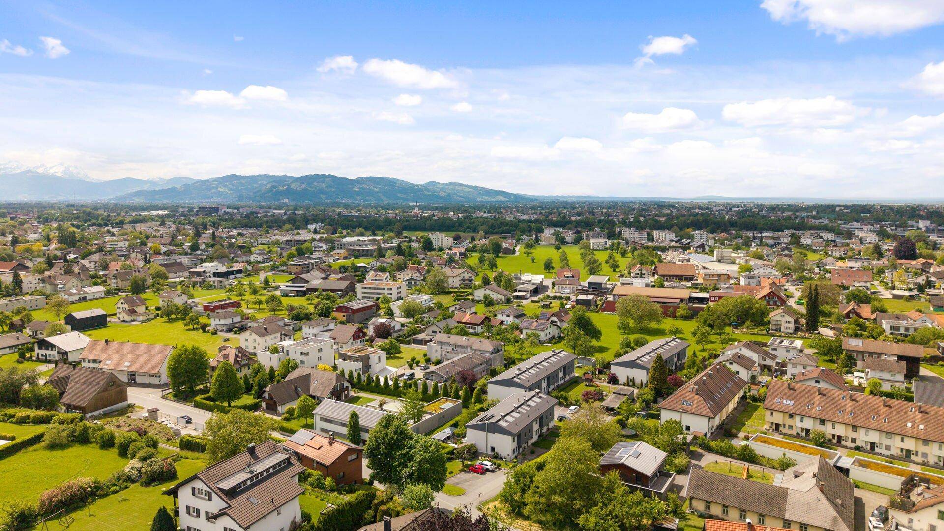Ausgedehnte Luftaufnahme einer Stadtlandschaft mit weitem Blick auf die umliegende Natur und Berge.