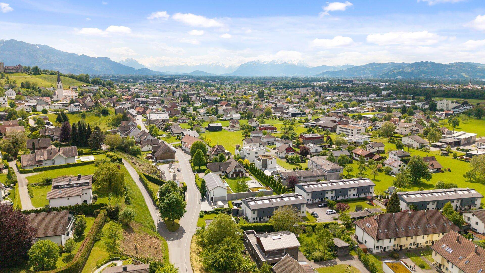 Malerische Luftaufnahme einer ländlichen Gemeinde mit Kirche, umgeben von grünen Hügeln und Bergen.