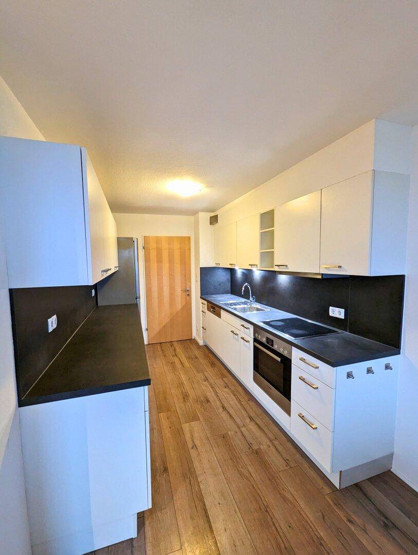 Moderne Küche mit weißen Schränken, dunklen Arbeitsplatten und Holzboden, ausgestattet mit Einbaugeräten.