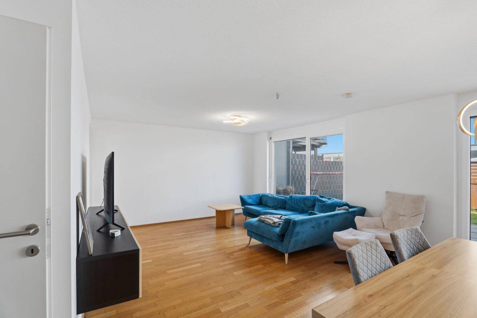 Geräumiges Wohnzimmer mit Holzboden, großem Fenster und viel natürlichem Licht.