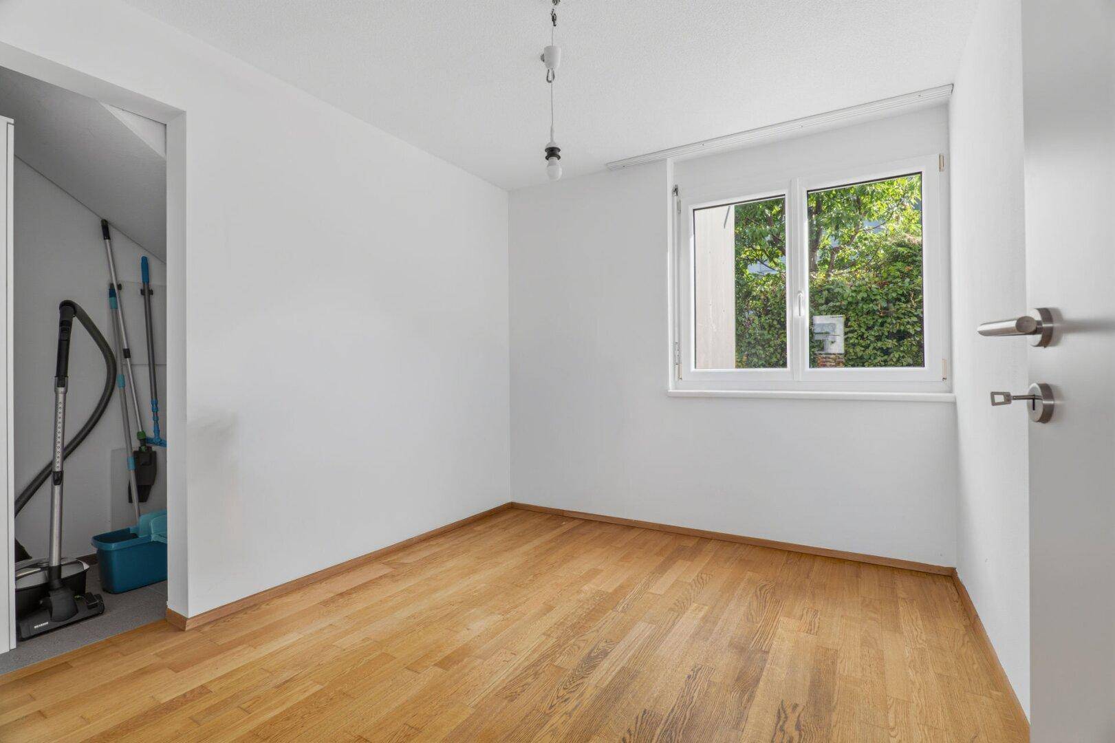 Kleiner Raum mit Holzboden, Fenster und Stauraum für Reinigungsgeräte.