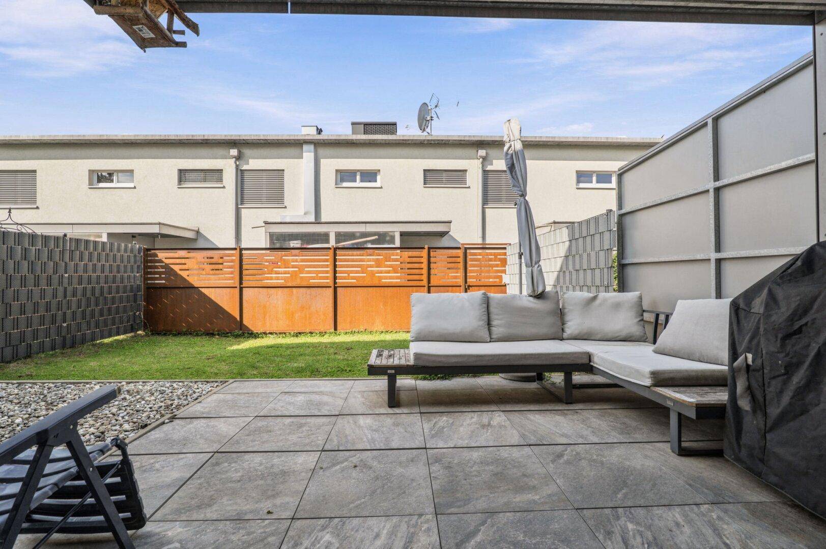 Geräumige Terrasse mit Sitzgelegenheiten und angrenzendem Rasenbereich.